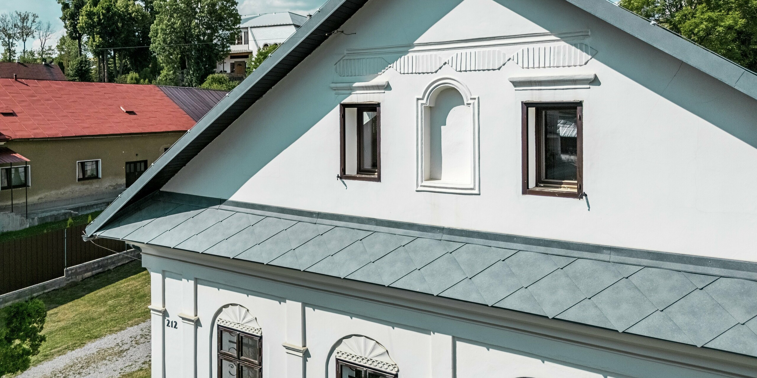 Die Nahaufnahme zeigt die Dachansicht des Handwerkerhauses in Klin, Slowakei, mit der PREFA Dachraute 44 × 44 in P.10 Steingrau. Das harmonische Zusammenspiel der modernen Dachdeckung mit der historischen Fassade unterstreicht den Charakter des Gebäudes. Besonders auffällig ist der scharfe Winkel des Dachs, der perfekt in die traditionelle Architektur integriert ist. Die farblich abgestimmten Dachrauten aus Aluminium bieten nicht nur eine ansprechende Optik, sondern sind auch korrosionsbeständig, leicht und langlebig. Diese Lösung bietet eine nachhaltige, funktionale und ästhetische Bereicherung für die Sanierung des Hauses.