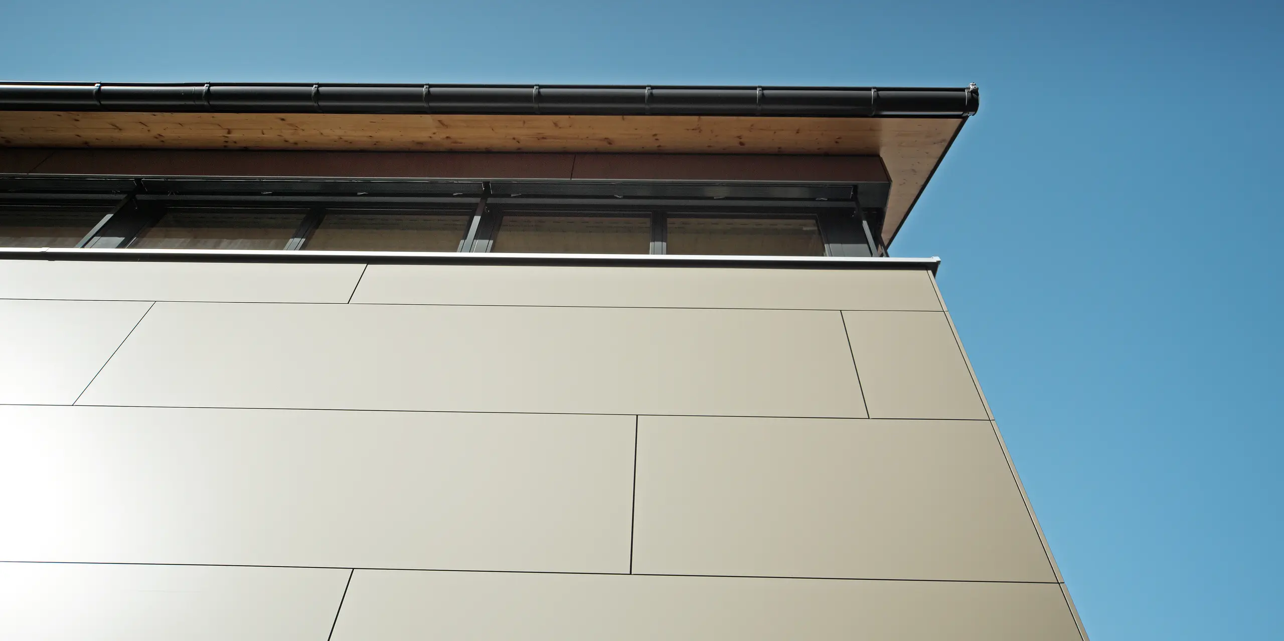 Detailaufnahme der Fassade eines Einfamilienhauses in Hohenems, ausgestattet mit PREFA Aluminium Verbundplatten in Bronzemetallic. Die präzise Montage zeigt keine sichtbaren Befestigungselemente, was die glatte und homogene Oberfläche betont. Die hochwertigen, korrosionsbeständigen Platten bieten durch ihre robuste Beschaffenheit und Farbbeständigkeit einen langlebigen Schutz und verleihen dem Haus eine moderne und einzigartige Optik.
