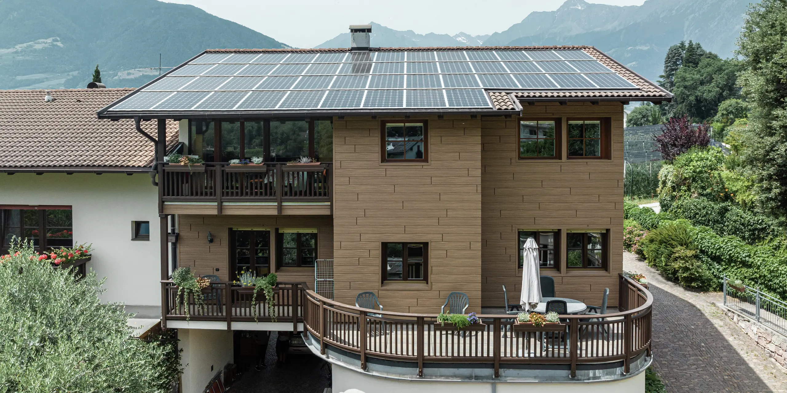 Appartements de vacances Prechtlhof rénovés à Merano, dans le Tyrol du Sud, avec Sidings PREFA en noyer foncé et une installation photovoltaïque à grande échelle sur le toit. La façade en aluminium à faible entretien et aspect bois allie durabilité et esthétique traditionnelle et s'intègre parfaitement dans le paysage alpin.