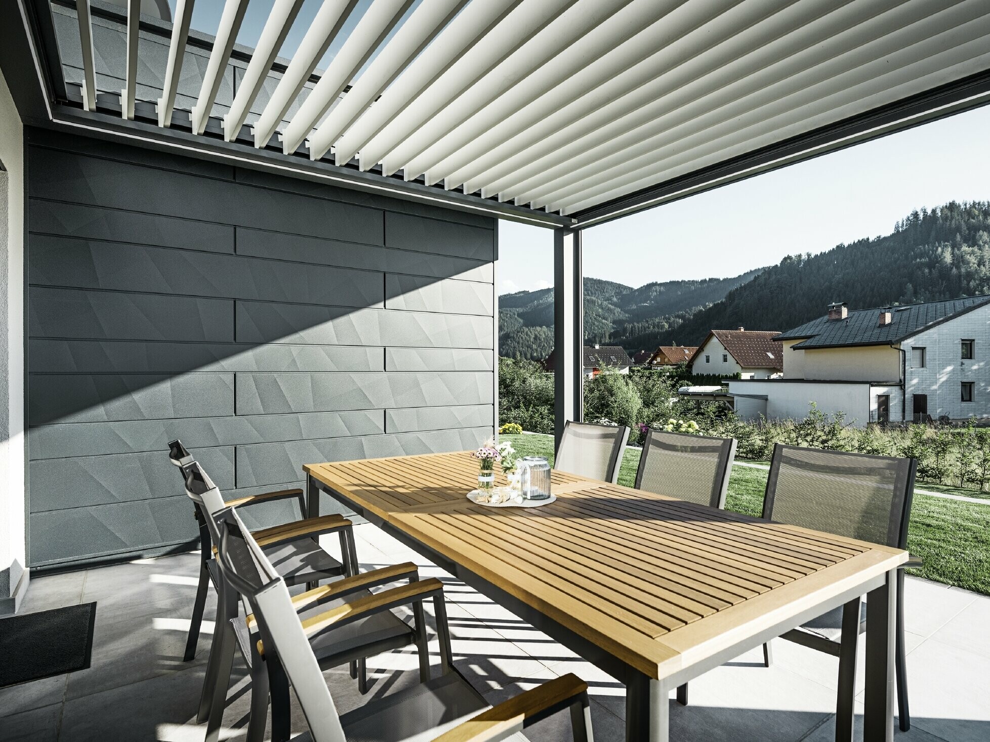 Terrasses couvertes de lamelles, protégées, avec table et fauteuils ; une façade est revêtue de panneaux de façade PREFA Siding.X anthracite.