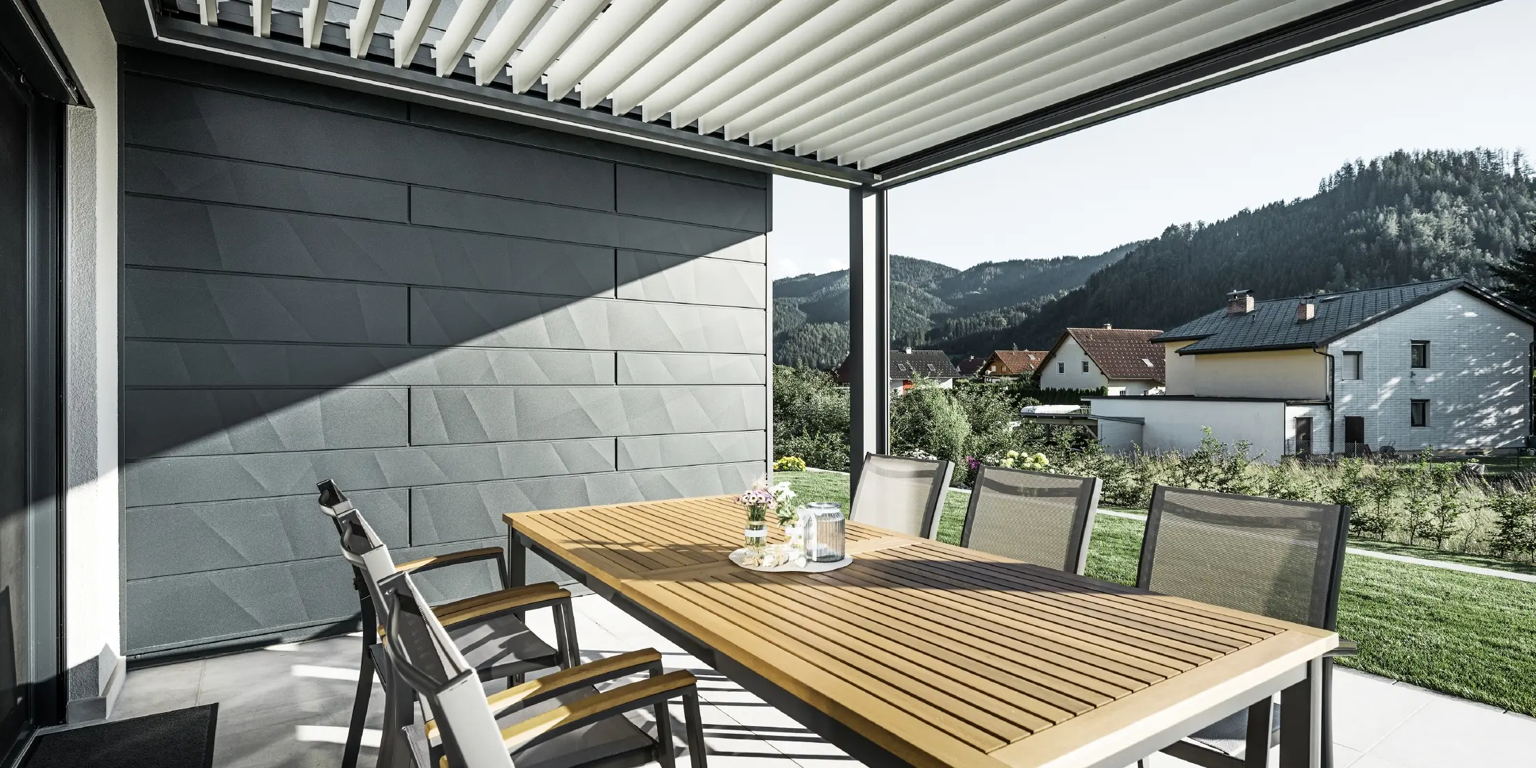 Terrasses couvertes de lamelles, protégées, avec table et fauteuils ; une façade est revêtue de panneaux de façade PREFA Siding.X anthracite.