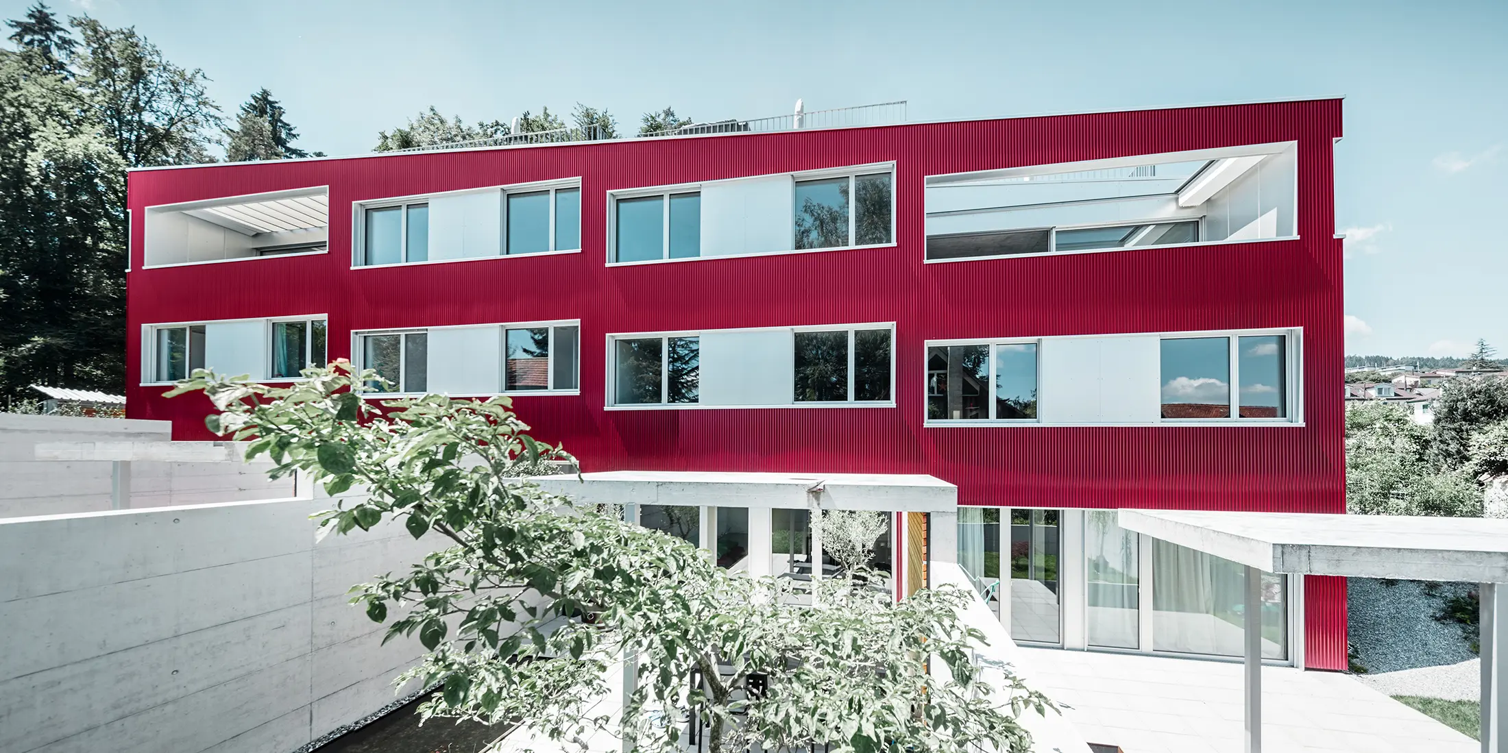 Wohnhausanlage mit Flachdach und Balkonen mit weinroter Fassade mit PREFA Welle