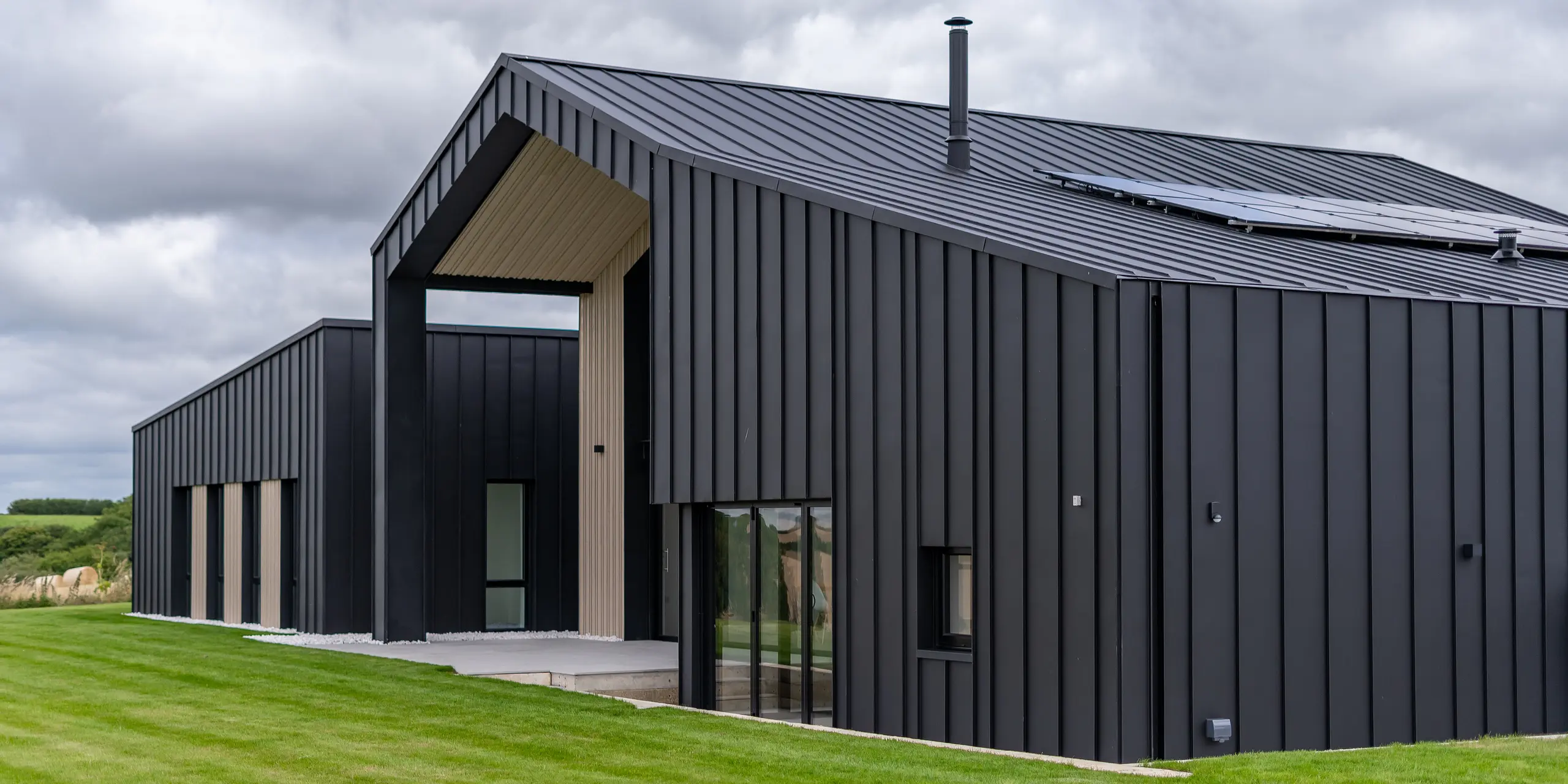 Vue oblique de l'arrière de « The Hide » à Cornwall avec toiture PREFALZ et revêtement de façade en P.10 Anthracite. L'aspect clair des joints debout du toit et de la façade en aluminium crée des lignes modernes et harmonieuses, complétées par des éléments en bois et la nature environnante - une interaction parfaite entre fonctionnalité et esthétique.
