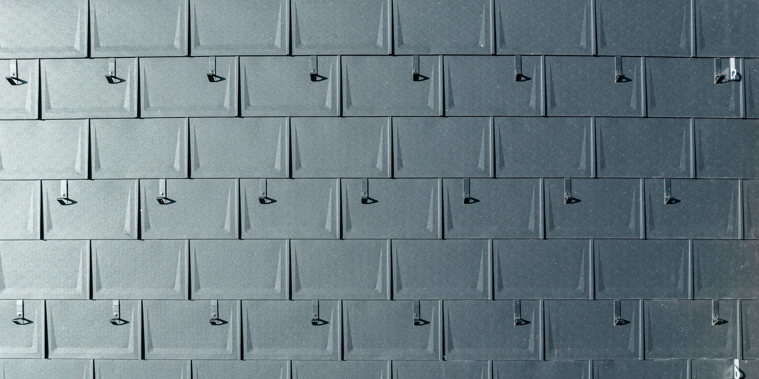 Gros plan d'une couverture de toit en aluminium PREFA. Les R.16 PREFA dans la couleur populaire P.10 anthracite sont reliés entre eux avec précision. Les panneaux en aluminium de haute qualité offrent une solution de toiture durable, résistante aux intempéries et visuellement attrayante. Les butées à neige offrent une sécurité supplémentaire.