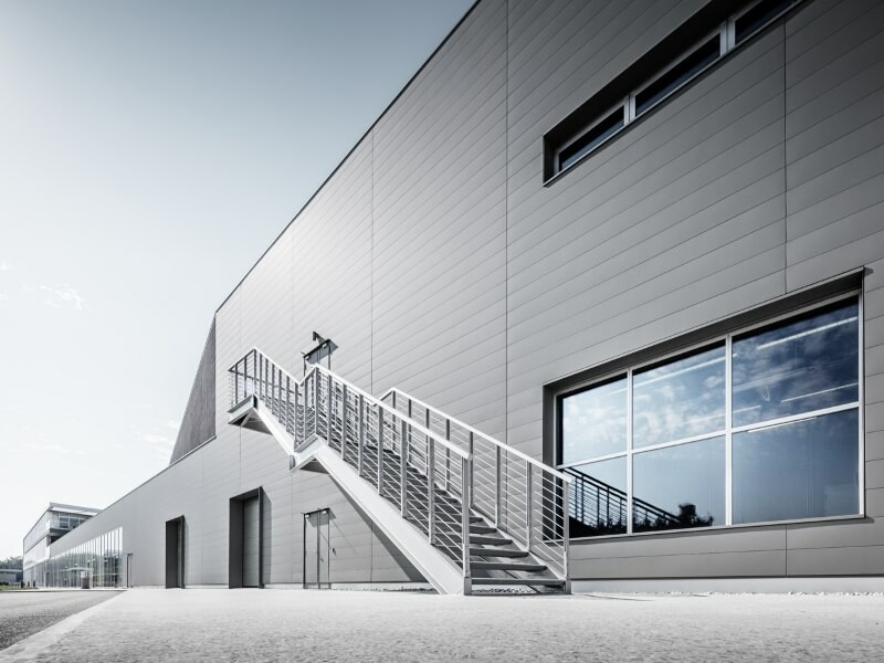 Vue de profil du nouveau centre de recherche Petronas à Turin (Italie). La façade a été réalisée avec le produit Siding dans 3 couleurs spéciales, P.10 Anthracite et P.10 Gris souris. Grâce à de larges fenêtres bâtiment profite pleinement de la lumière du jour. Les escaliers permettent d'accéder au bâtiment depuis le côté de la façade.