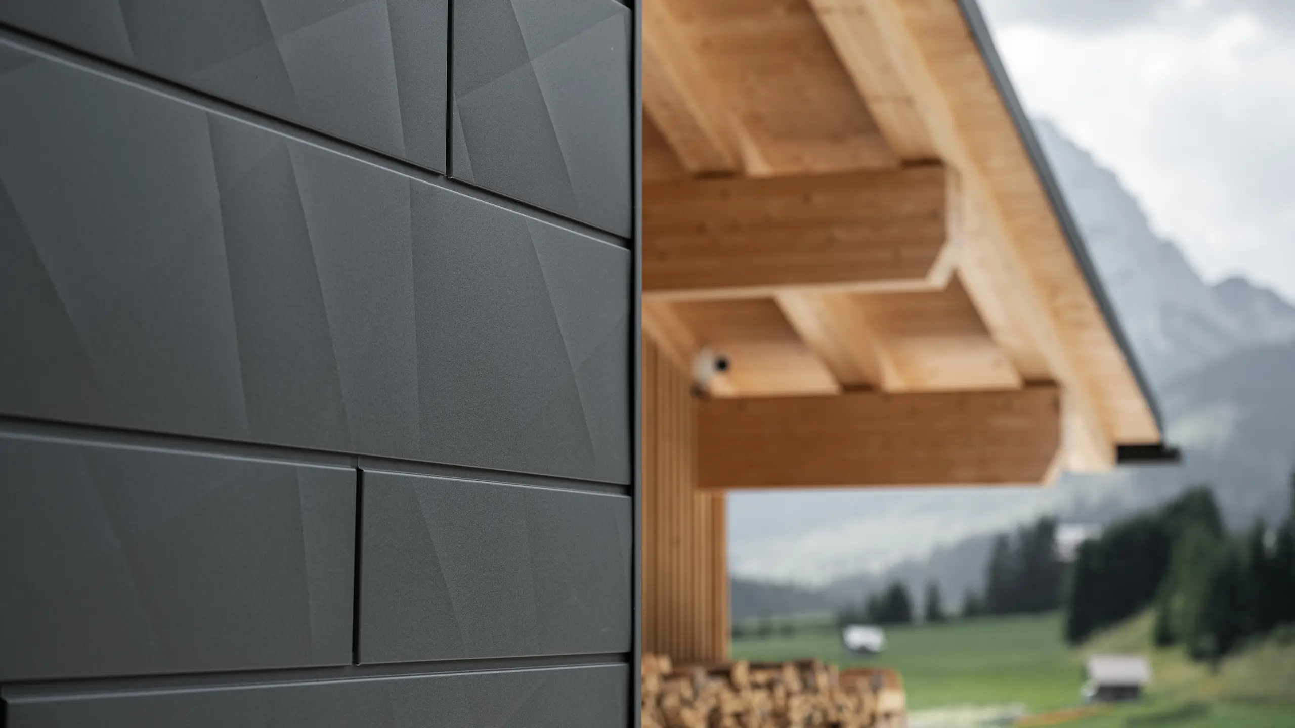 Gros plan sur les panneaux de façade Siding.X en P.10 noir de PREFA à la Casa Hoffe à Sappada, Italie. Le système de façade en aluminium au design moderne et abstrait, crée un contraste intéressant avec les éléments apparents de la charpente en bois. Cette solution de façade innovante, qui s'intègre harmonieusement à l'environnement alpin, combine fonctionnalité, durabilité et culture architecturale esthétique.