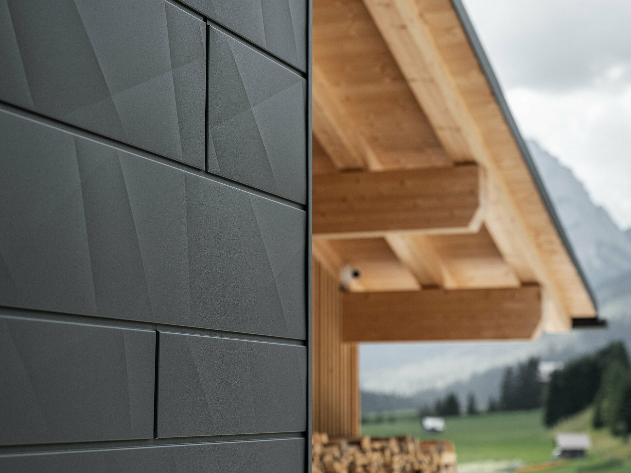Gros plan sur les panneaux de façade Siding.X en P.10 noir de PREFA à la Casa Hoffe à Sappada, Italie. Le système de façade en aluminium au design moderne et abstrait, crée un contraste intéressant avec les éléments apparents de la charpente en bois. Cette solution de façade innovante, qui s'intègre harmonieusement à l'environnement alpin, combine fonctionnalité, durabilité et culture architecturale esthétique.