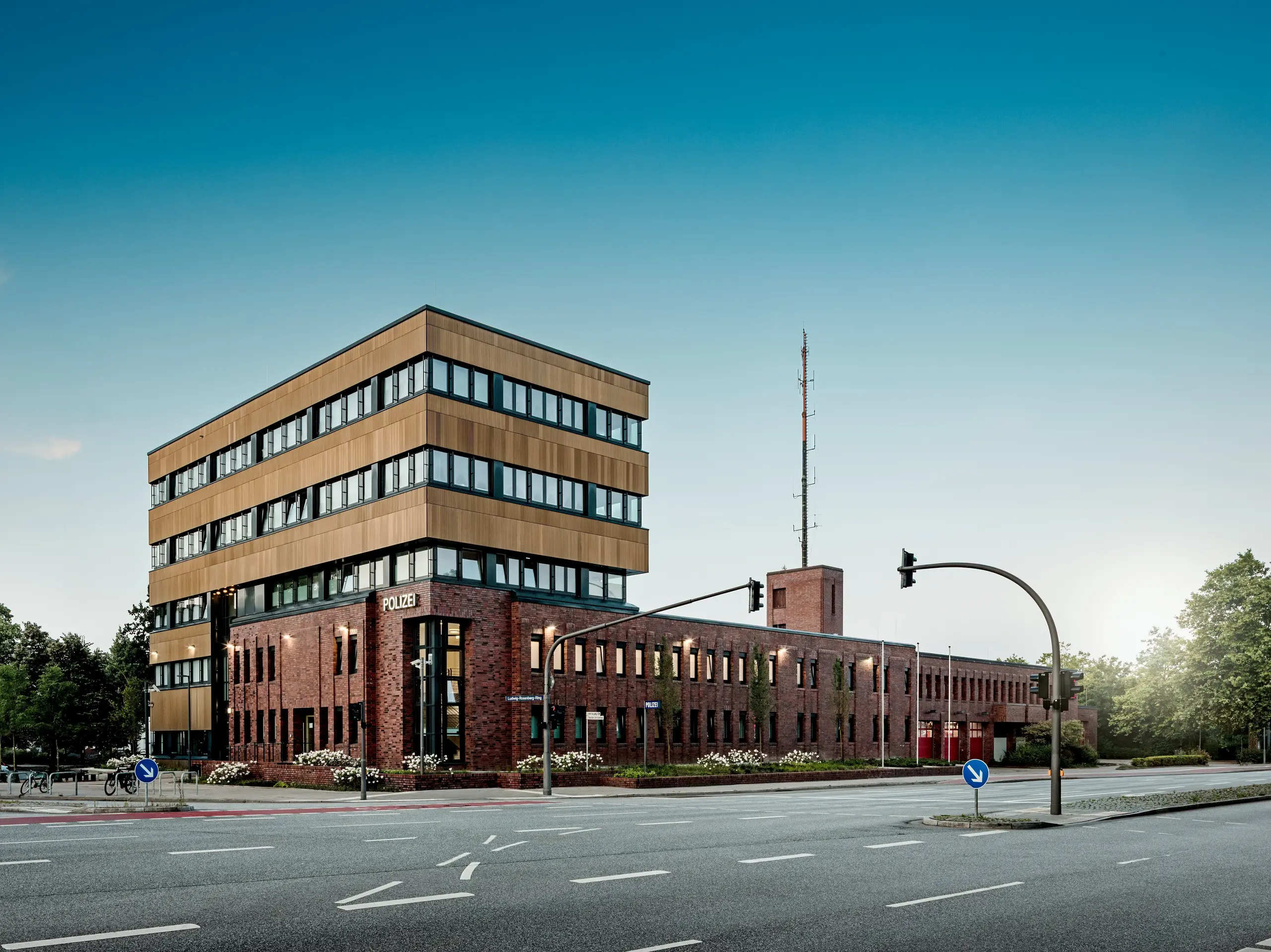 Vue panoramique du commissariat 43 à Hambourg : ce nouveau bâtiment à la structure précise domine les immeubles en briques existants et séduit par sa façade en aluminium PREFA, composée de profils extrudés « triangle » couleur bronze moyen. La superposition horizontale et la surface finement texturée créent des reflets vibrants selon l’angle de la lumière, faisant de ce bâtiment un véritable chef-d’œuvre architectural. L’aluminium PREFA impressionne par sa haute résistance à la corrosion, sa durabilité et ses exigences minimales d’entretien : une solution durable pour des façades modernes, fonctionnelles et élégantes.