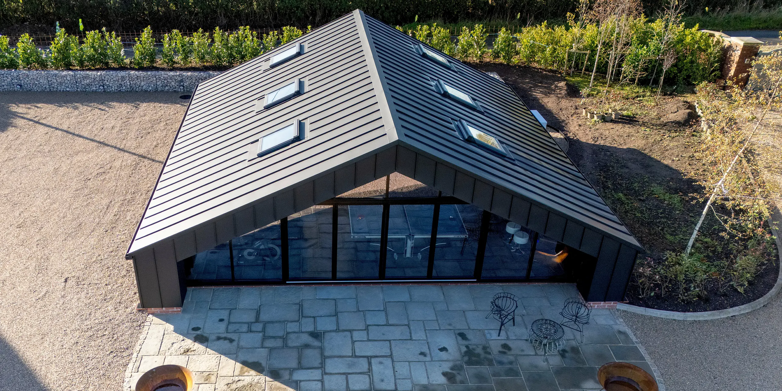 Vue aérienne d'un bâtiment de loisirs moderne, revêtu d'une enveloppe en aluminium PREFA et d'une toiture PREFALZ P.10 Noir. La forme épurée et symétrique de la toiture, la large façade vitrée et l'extérieur structuré lui confèrent une allure dynamique et haut de gamme. La surface en aluminium résistant aux intempéries garantit une stabilité durable et une précision architecturale irréprochable.