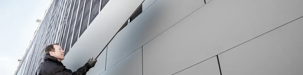 Photos d'une façade partiellement achevée, habillée avec des Siding PREFA en largeur 500. Le couvreur installe un autre panneau de façade. La vue a été prise d'en bas. 