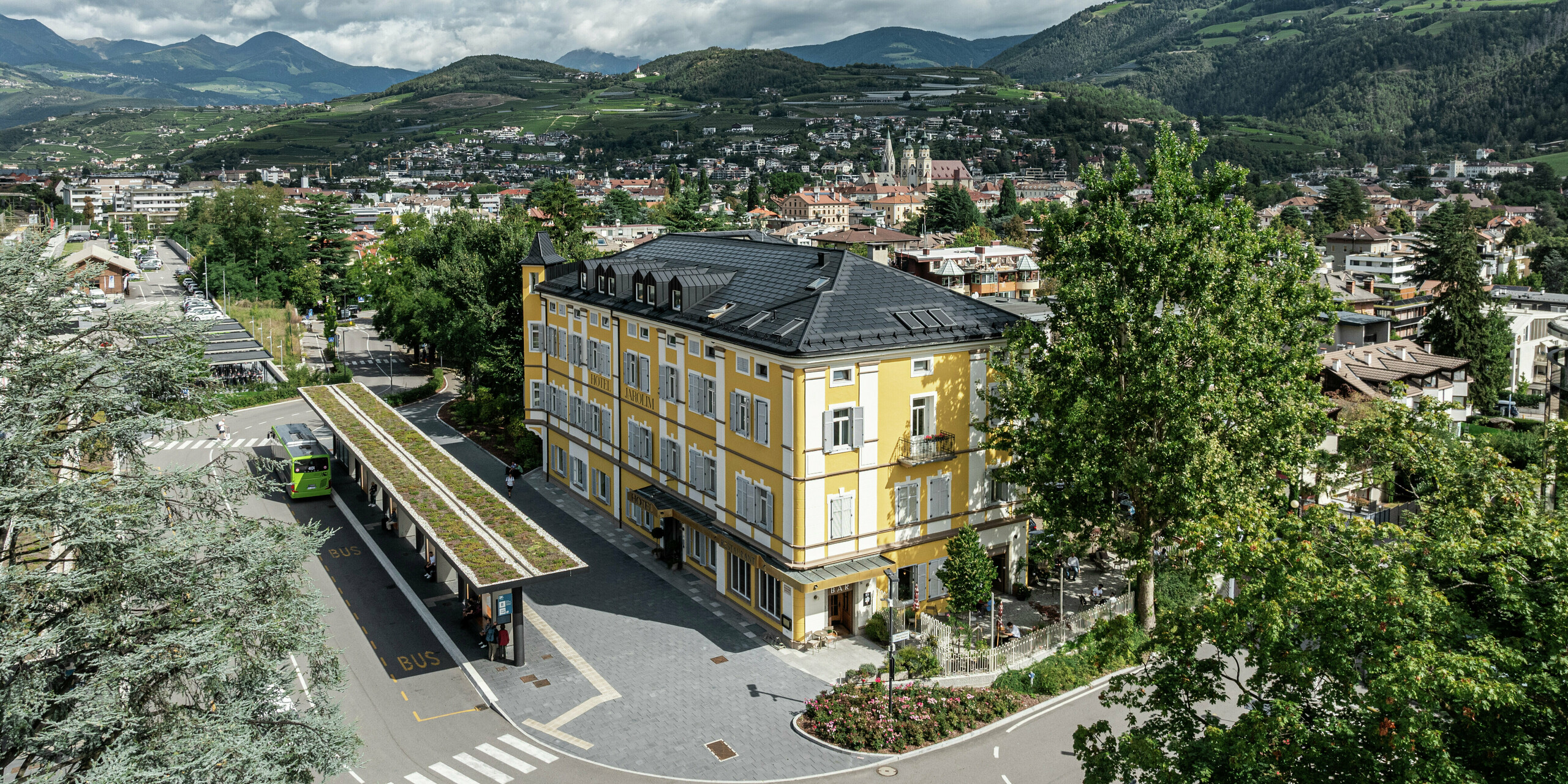 Vue panoramique de l'Hôtel Jarolim à Brixen, équipé d'un toit PREFA moderne composé de tuiles solaires et de R.16. Le toit en aluminium durable et résistant aux intempéries combine une production d'énergie durable avec une esthétique élégante et s'intègre harmonieusement dans l'architecture classée du bâtiment. Entouré par le paysage pittoresque du Tyrol du Sud, l'hôtel montre comment tradition et innovation peuvent être parfaitement combinées.