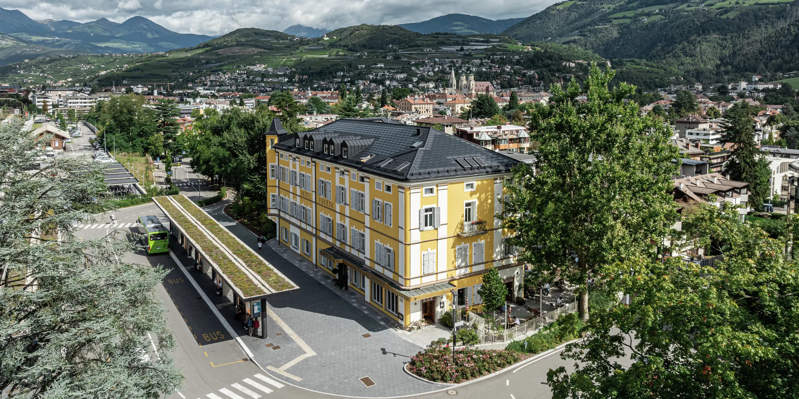 Vue panoramique de l'Hôtel Jarolim à Brixen, équipé d'un toit PREFA moderne composé de tuiles solaires et de R.16. Le toit en aluminium durable et résistant aux intempéries combine une production d'énergie durable avec une esthétique élégante et s'intègre harmonieusement dans l'architecture classée du bâtiment. Entouré par le paysage pittoresque du Tyrol du Sud, l'hôtel montre comment tradition et innovation peuvent être parfaitement combinées.