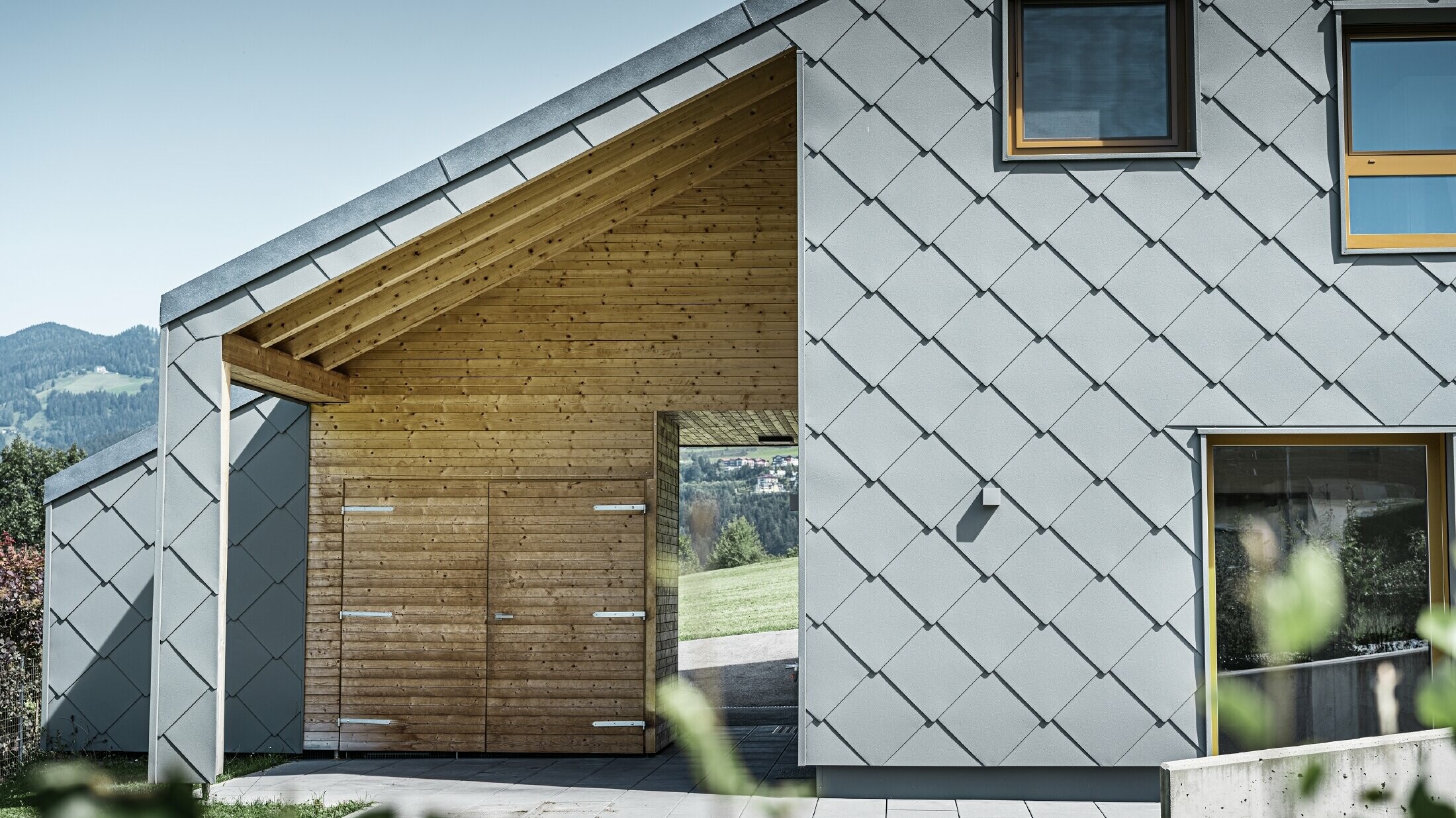 L’entrée couverte est faite de boiseries horizontales ; le reste de la façade est revêtu du losange de façade grand format PREFA en aluminium gris souris