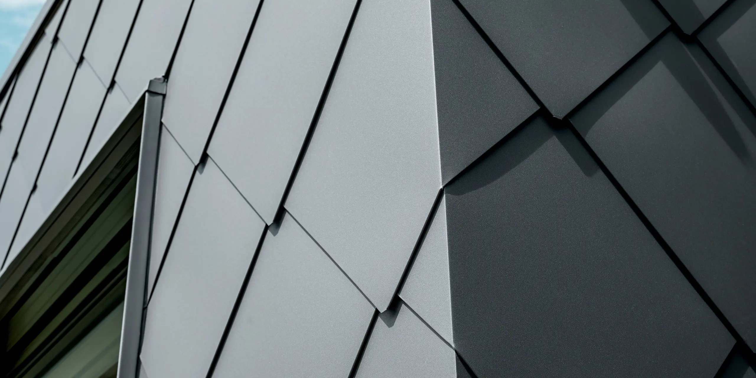 Gros plan sur les losanges de toiture et de façade 44x44 PREFA, couleur P.10 gris sombre, d'une maison individuelle à Trnava-Modranka. L'image révèle la précision de la pose du motif en losange, dont les lignes et les arêtes nettes mettent particulièrement en valeur la qualité de l'aluminium. La surface mate crée d'élégants reflets et confère à la façade une allure moderne et technique. Durables, les produits en aluminium PREFA offrent une résistance maximale aux intempéries, une grande stabilité et une apparence uniforme, pour une architecture remarquable et intemporelle.