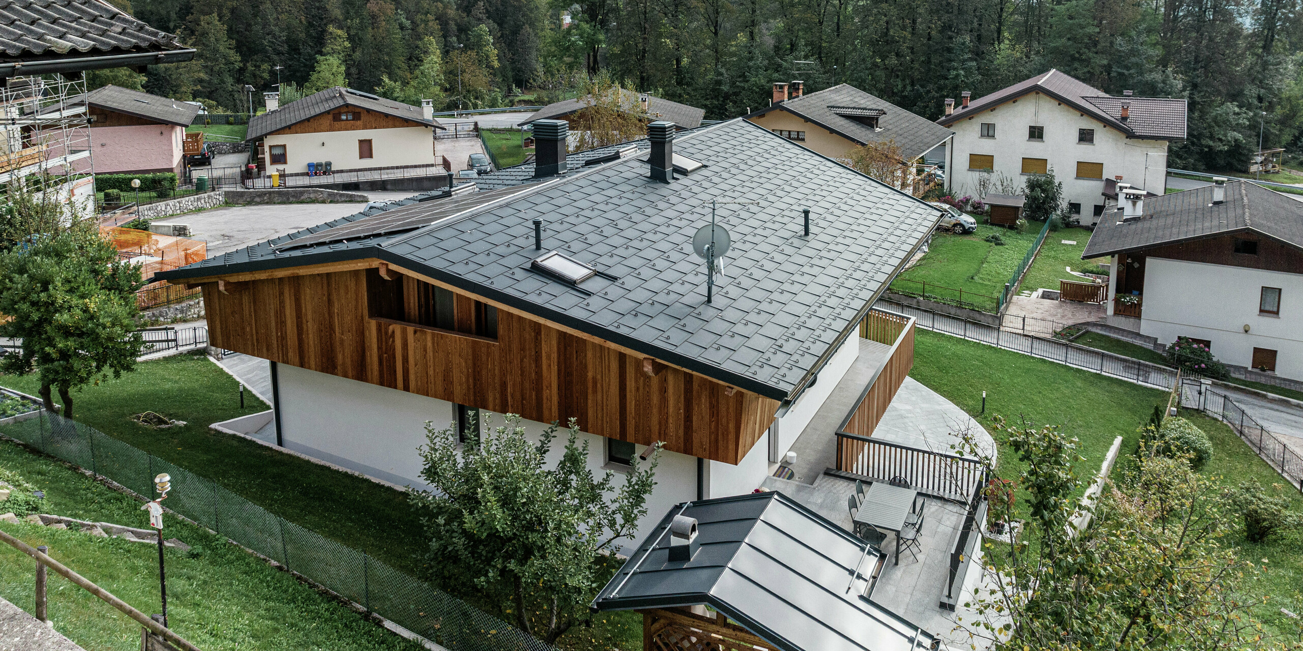 Saniertes Einfamilienhaus in Agordo, Italien, mit widerstandsfähigem Aluminiumdach. Die PREFA Dachplatte R.16 in P.10 anthrazit bietet optimalen Witterungsschutz und fügt sich harmonisch in die Umgebung ein. Die PREFA Dachentwässerung mit Kastenrinne und Ablaufrohr sorgt für eine effiziente Wasserableitung. Die Kombination aus naturbelassener Holzfassade im Obergeschoss, weißer Putzfassade im Erdgeschoss und hochwertigem Aluminium im Dachbereich verleiht dem Gebäude eine stilvolle und moderne Optik.