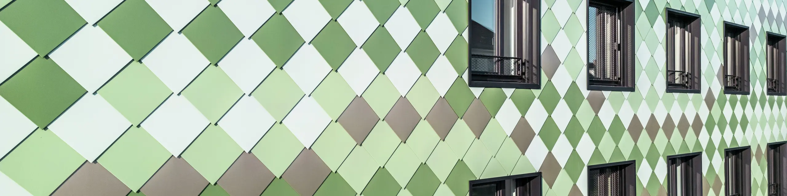 Moderne PREFA-Fassadenverkleidung mit PREFA-Rhombusen in den speziell entwickelten Sonderfarben Olivgrün, Graugrün, Resedagrün, Opalgrün, Hellelfenbein, Perlweiß und Hellbronze. Das Wohn- und Geschäftsgebäude „Pick-Nick“ in Dresden besticht durch seine einzigartige Ästhetik, Witterungsbeständigkeit, Langlebigkeit und Wartungsfreiheit. Das stilvolle Design und die Farbvielfalt setzen architektonische Akzente und bieten nachhaltigen Schutz.