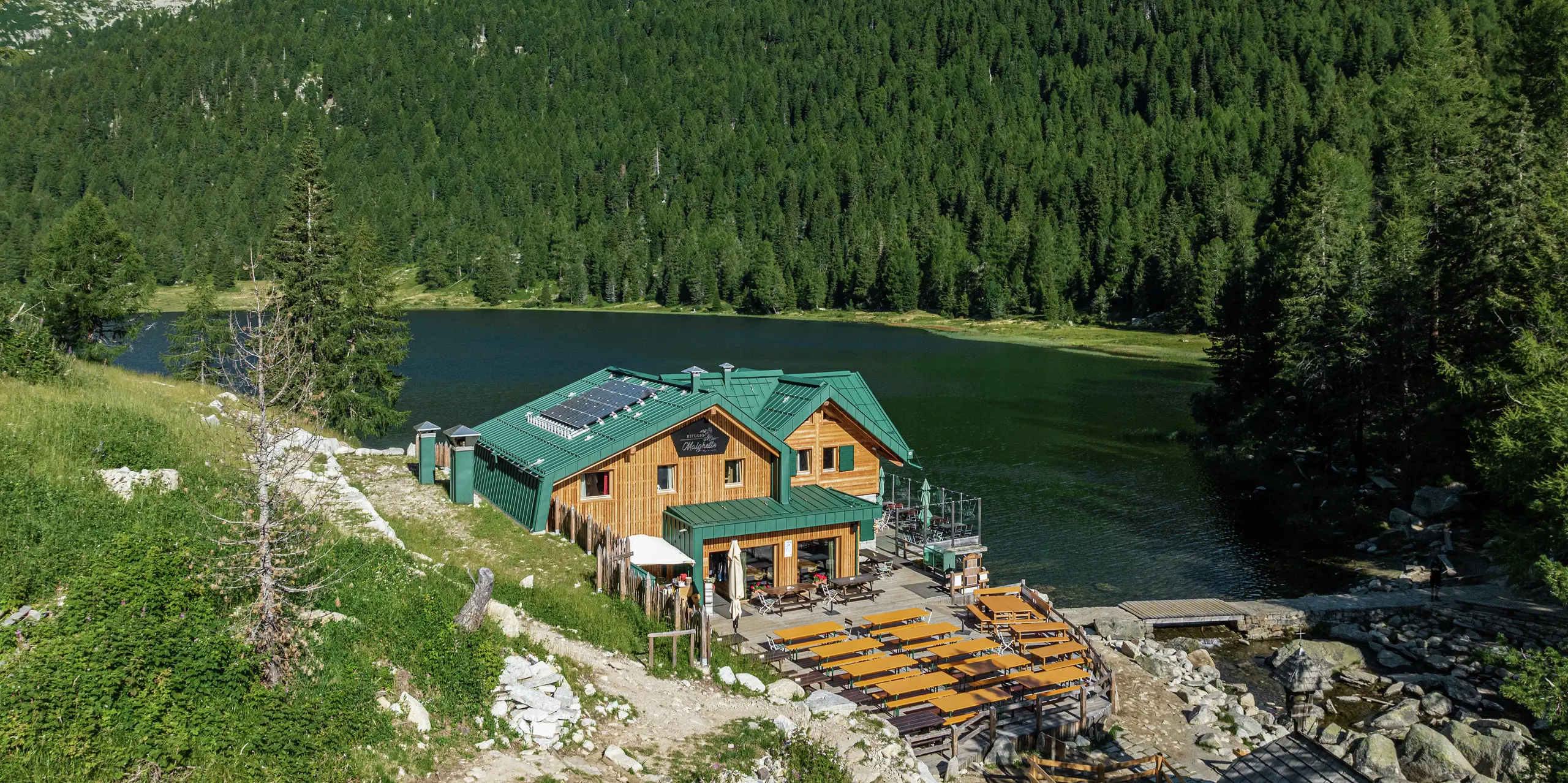 Le Rifugio Malghette à 1 888 m, idéalement situé au bord du lac, avec le toit PREFALZ en vert mousse P.10 - résistant aux intempéries, durable et parfaitement intégré dans la nature. La spacieuse terrasse ensoleillée invite les randonneurs à s'attarder et le toit en aluminium durable résiste même aux conditions météorologiques extrêmes en montagne.