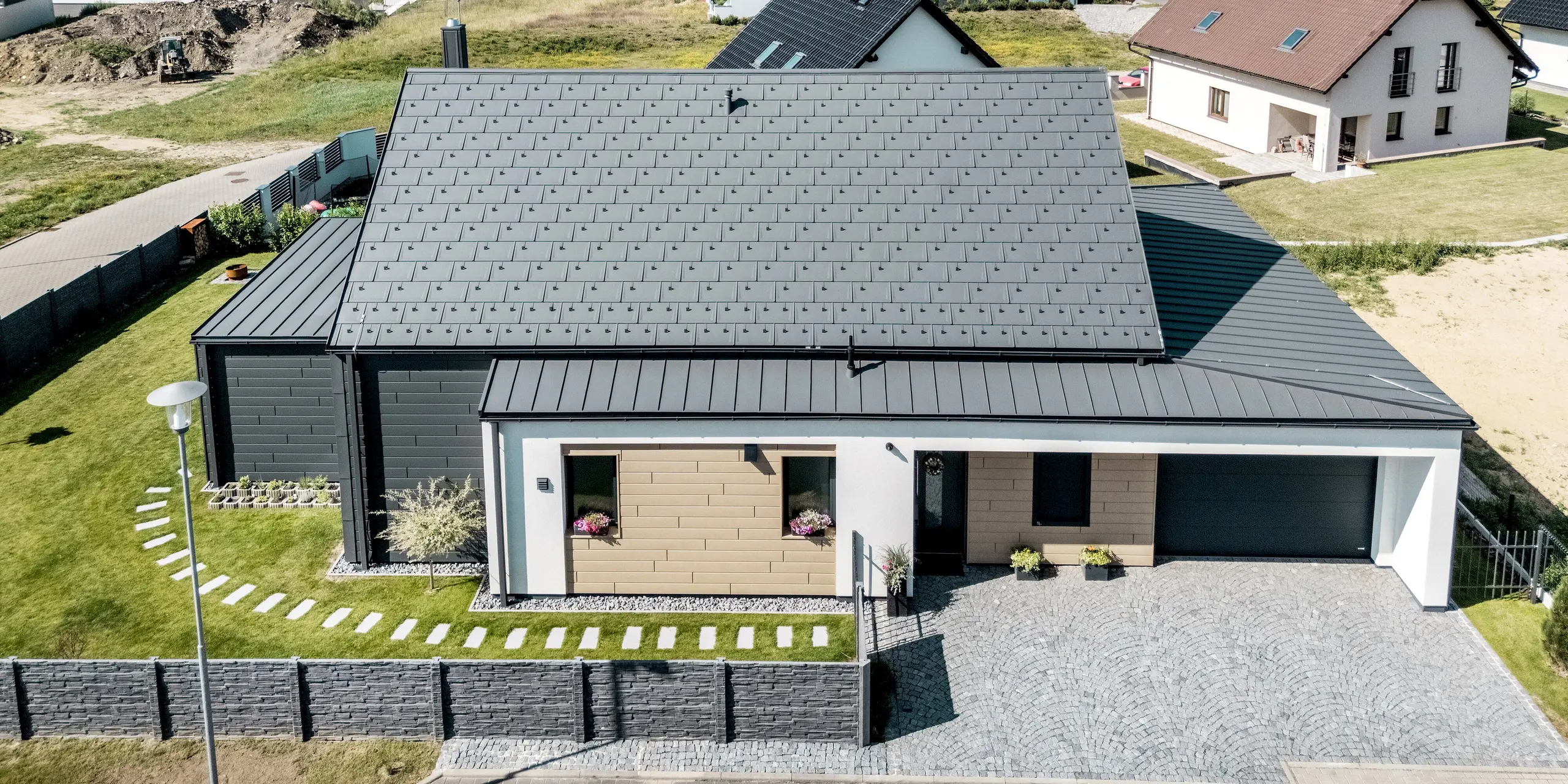 Luftaufnahme des Einfamilienhauses in Hlinsko mit moderner PREFA Aluminium-Gebäudehülle. Die großflächige Dachfläche mit PREFA Dachplatte R.16 und PREFALZ in P.10 Dunkelgrau sowie die abgestimmte Fassadengestaltung mit Sidings und PREFALZ zeigen ein harmonisches Zusammenspiel von Form und Farbe. Die langlebigen Aluminiumprodukte fügen sich elegant in die Umgebung ein und bieten zuverlässigen Schutz, Stabilität und zeitlose Ästhetik.