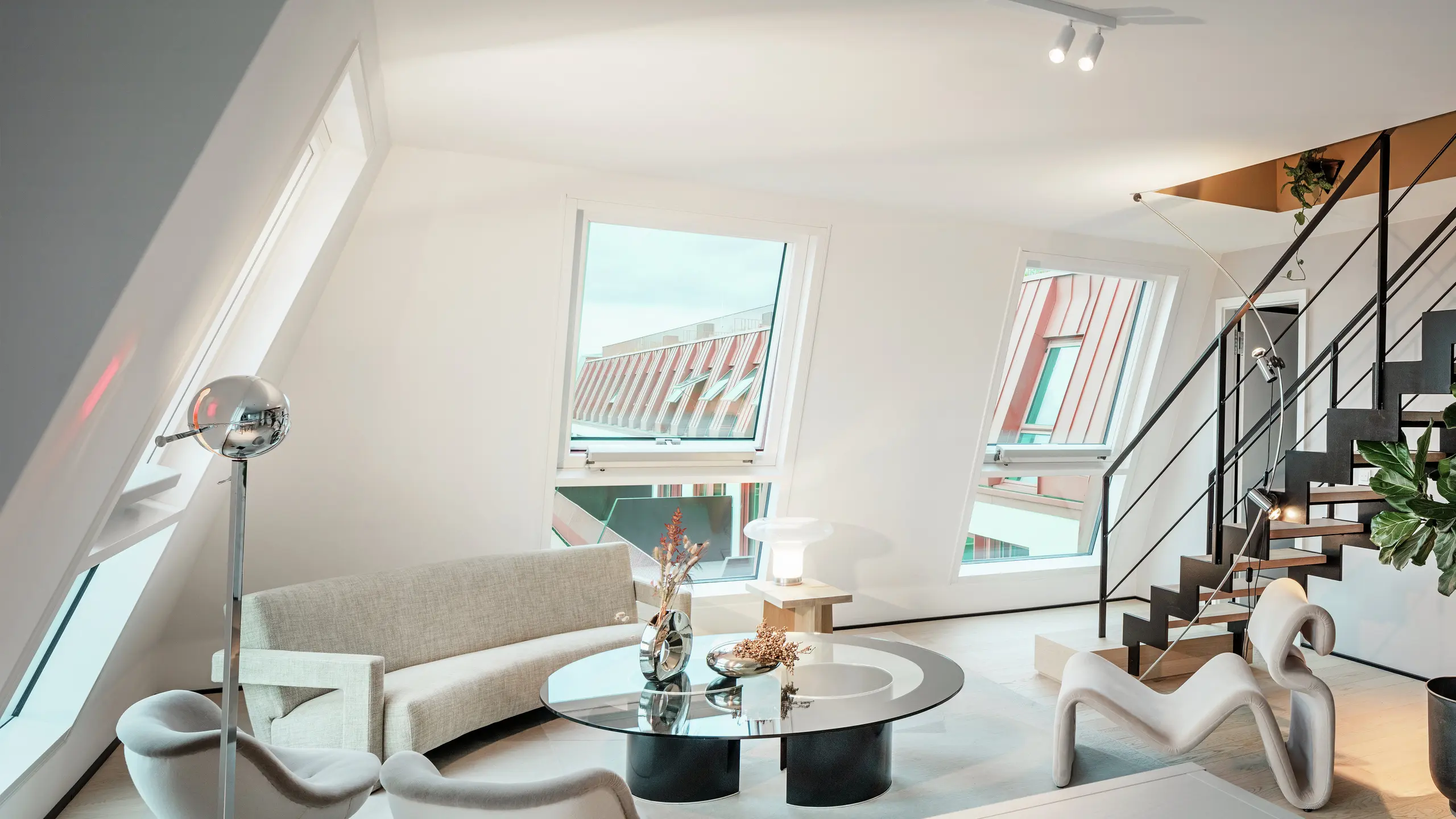 Innenansicht des lichtdurchfluteten Penthouses im Wohnprojekt Van B in München mit Blick auf das hochwertige PREFALZ-Aluminiumdach in der Sonderfarbe IGP Orange HDP. Große Glasflächen lassen viel Tageslicht herein und unterstreichen das moderne Wohnkonzept. Klare Linien, Designermöbel und die präzise Ausführung der Dachverbindungen zeigen, wie hochwertige und stilvolle Architektur nicht nur außen, sondern auch innen realisiert werden kann.