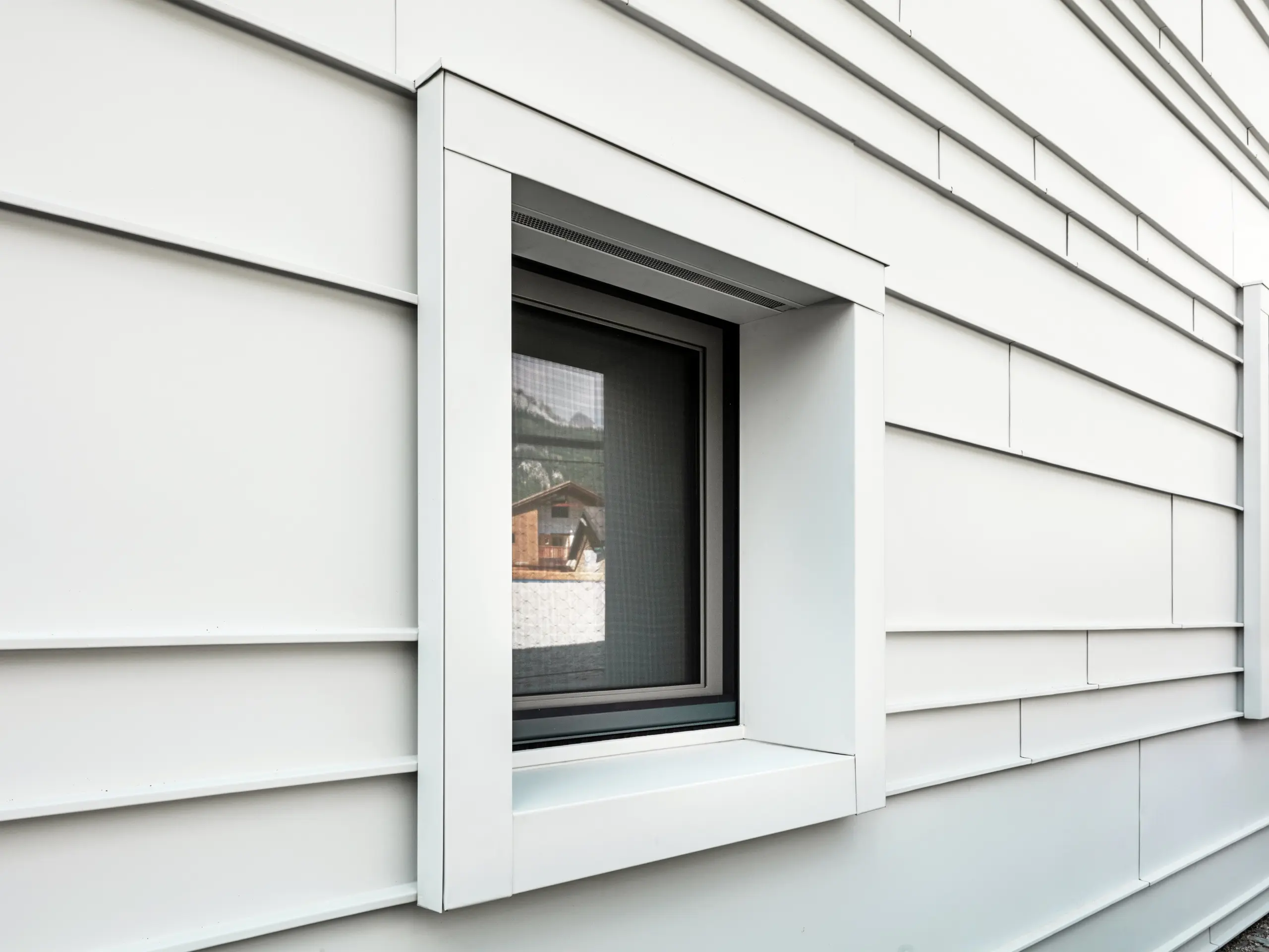Détail d'une fenêtre caractéristique dans une façade ventilée en PREFALZ P.10 couleur blanc Prefa. Les lames d'aluminium posées horizontalement apportent structure, clarté et esthétique moderne. Les cadres de fenêtres très saillants de la caserne « Tempesti » commencent et se terminent toujours exactement au niveau d'une ligne de pli. Cela permet de mettre délibérément en valeur la structure de l'aluminium.