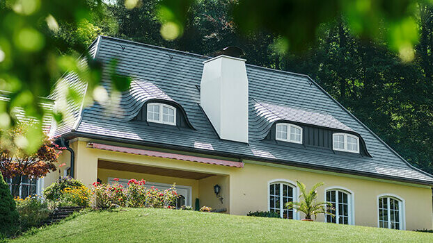 Einfamilienhaus mit neu saniertem Dach mit der PREFA Dachschindel in Anthrazit mit gerundeten Gauben (Fledermausgaube) und weißem Kamin.