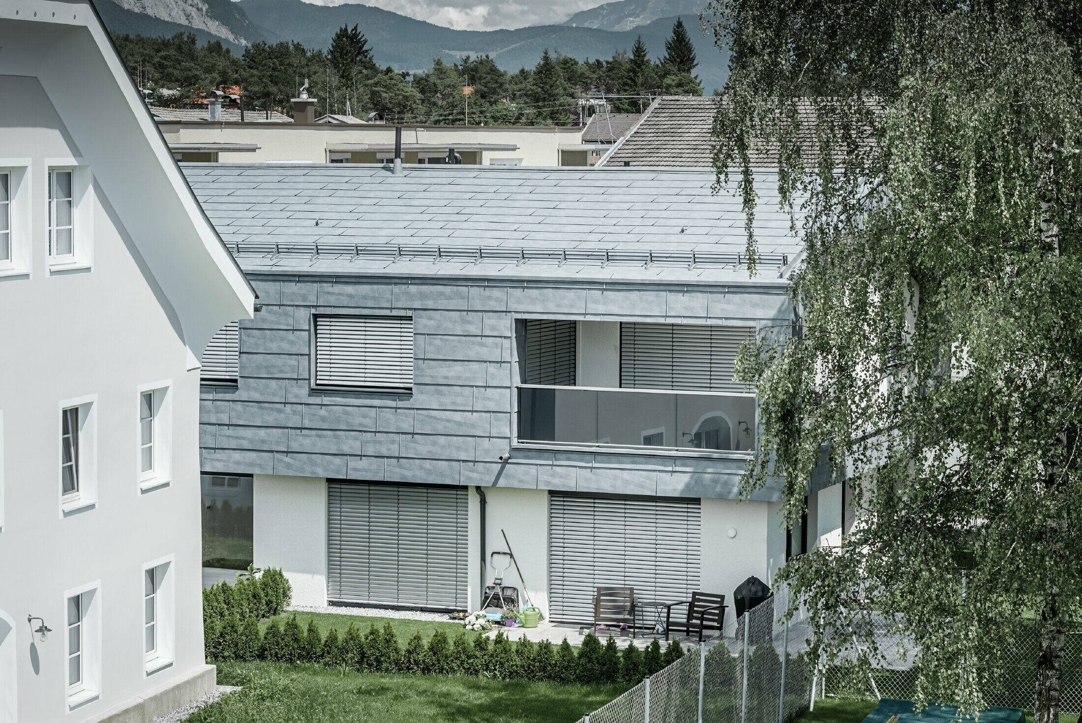 Maison individuelle classique avec toit à deux pans et deux lucarnes, recouverte de panneaux de toiture FX.12 PREFA couleur gris pierre.