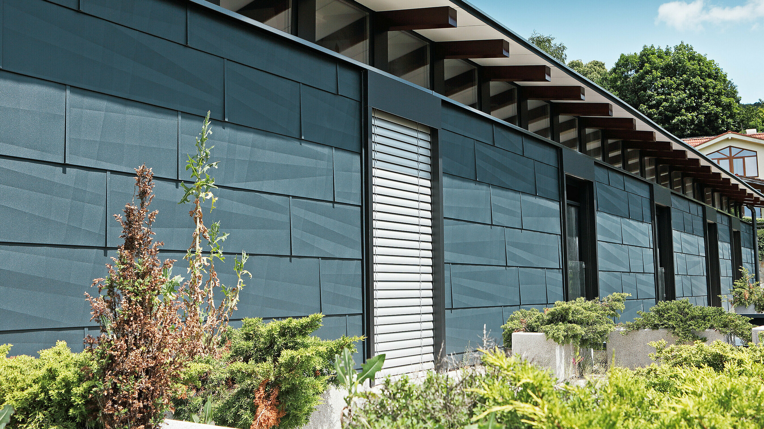 Côté exposé aux intempéries et donnant sur un jardin d’aspect moderne grâce au panneau de façade FX.12 couleur anthracite.