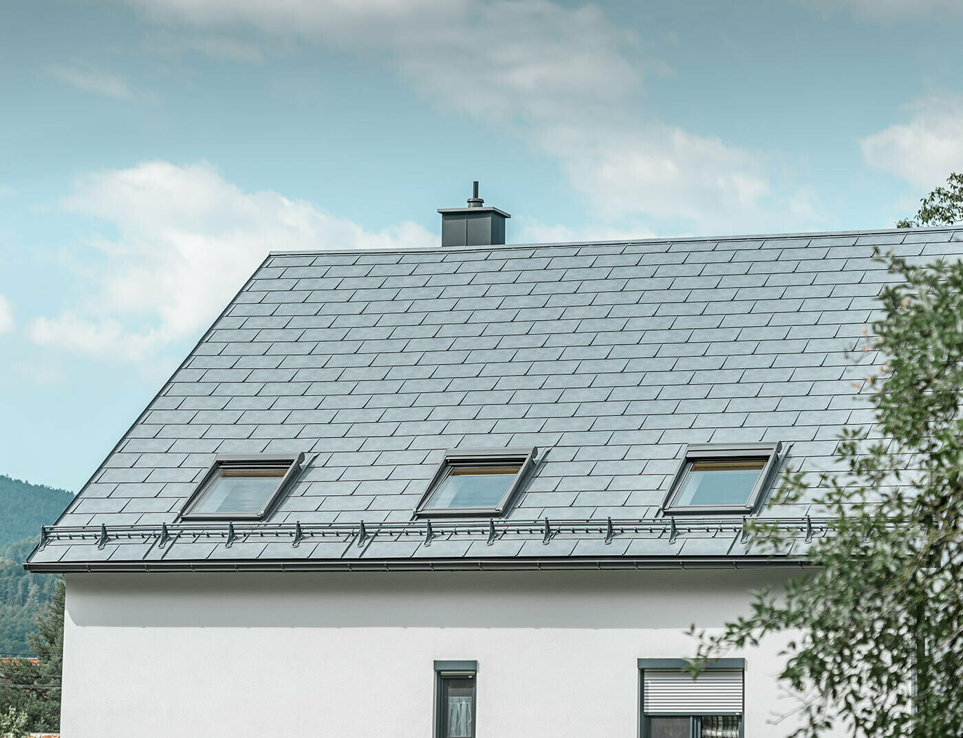 Maison individuelle classique avec toit en pente et trois fenêtres de toit, recouverte de R.16 en gris pierre et d'une façade en plâtre blanc