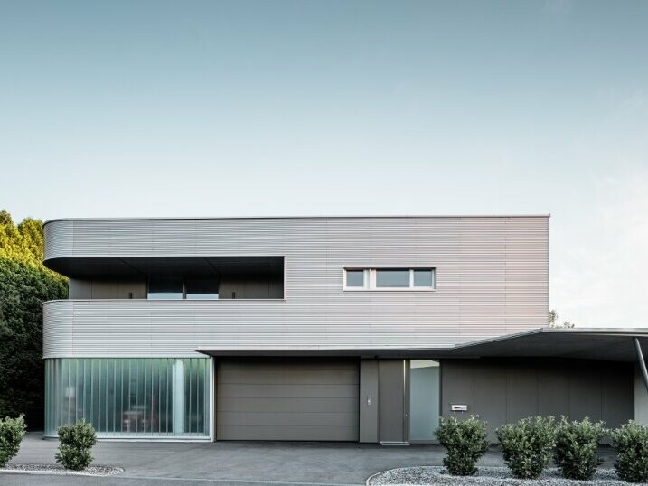 Vue de face de la maison de Leonding dont la façade est recouverte avec les profils sinus PREFA dans la teinte aluminium anodisé naturel.