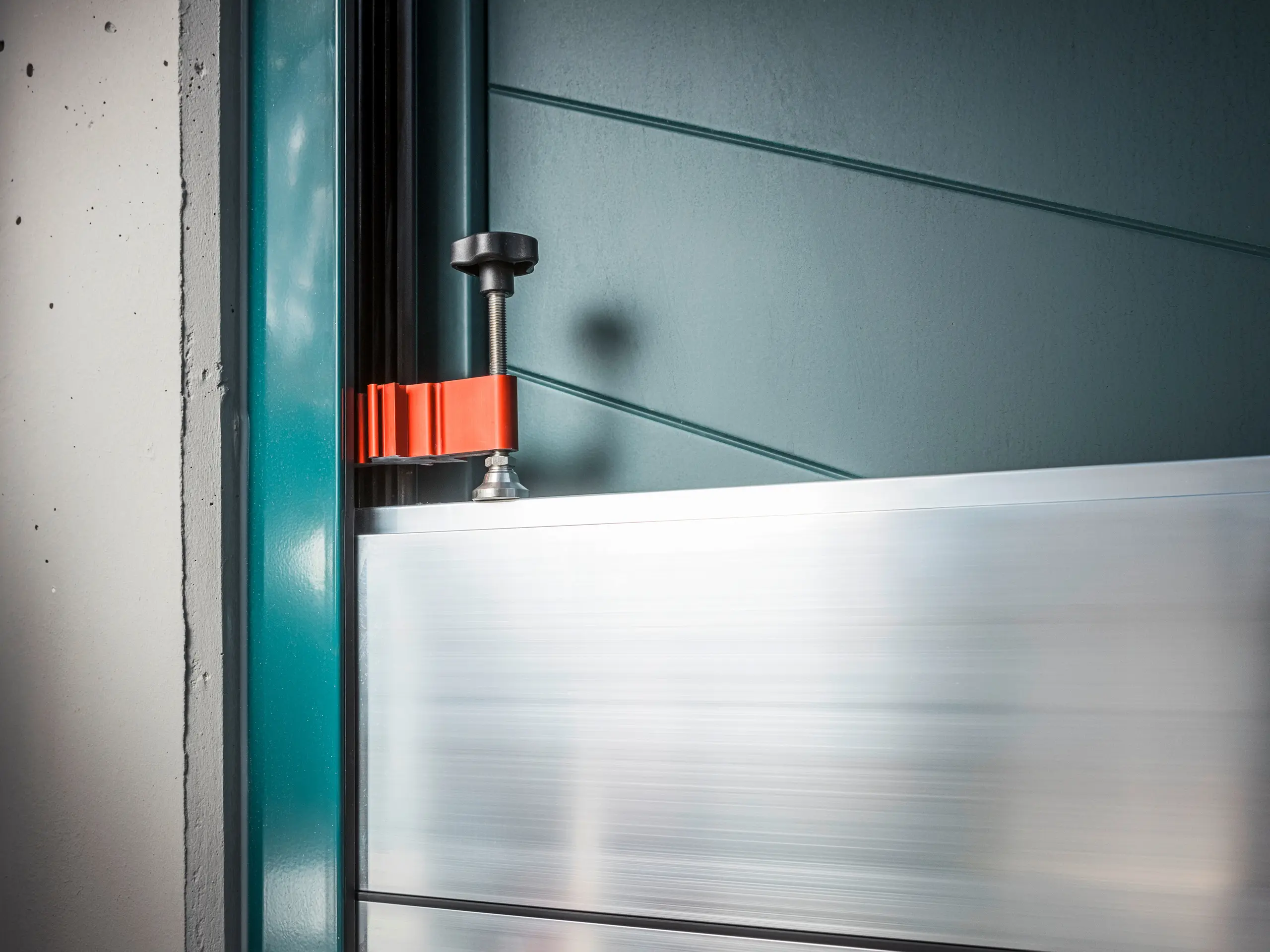 Détail du système de protection contre les crues PREFA sur un cadre de porte, composé de batardeaux en aluminium fixés par une pince rouge robuste (la pièce de serrage) pour garantir une protection sûre contre les crues.