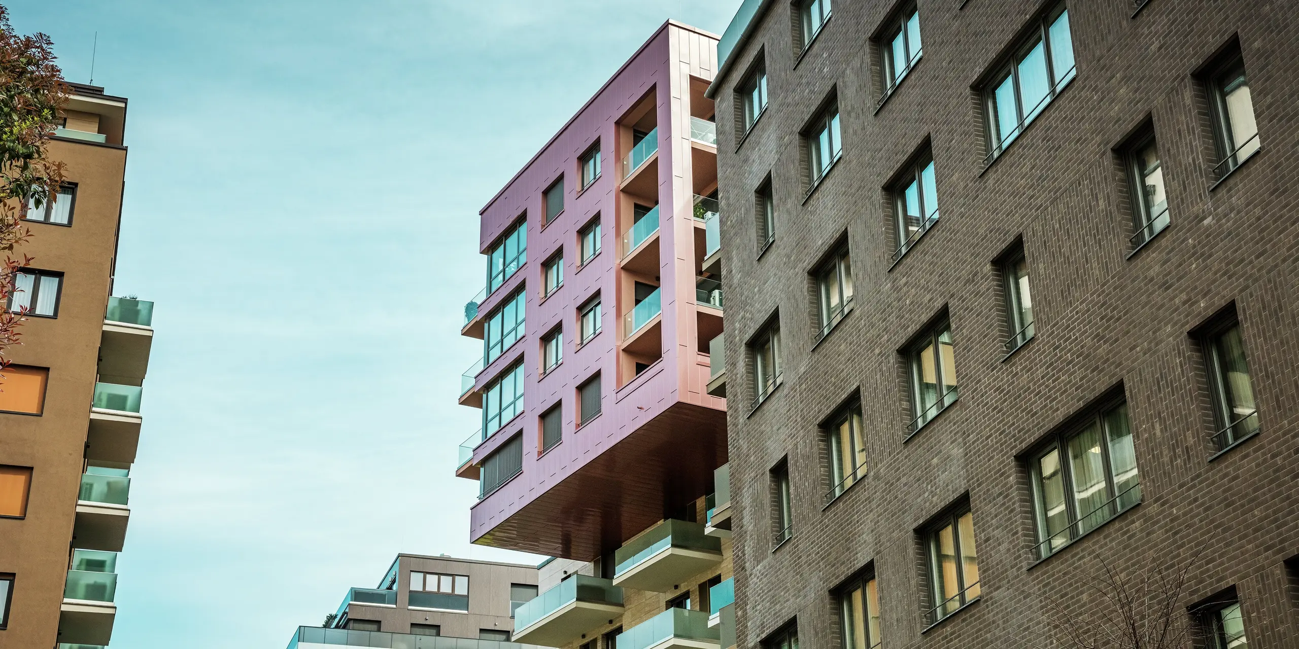 Vue de l'impressionnant bâtiment en porte-à-faux du projet Grand Corvin, dans le quartier Corvin de Budapest. Les étages supérieurs sont revêtus de panneaux de façade Siding PREFA, posés verticalement et d'une finition saumon métallisé particulière. La façade en aluminium robuste se détache nettement de l'architecture en briques environnante et souligne le caractère architectural moderne du quartier revitalisé.