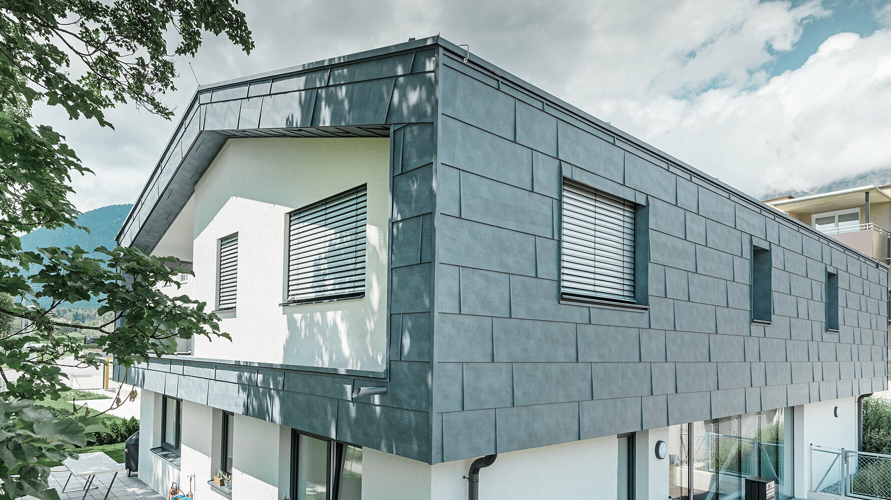 Modernes Einfamilienhaus ohne Dachvorsprung; Die obere Etage wurde mit PREFA Fassadenpaneelen FX.12 in Steingrau verkleidet, der Rest der Fassade wurde weiß verputzt.