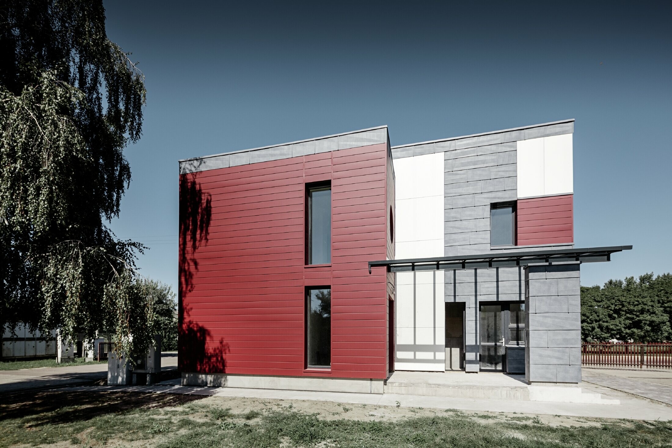 Complexe de bureaux moderne — Façade tricolore (blanc, rouge et gris pierre) réalisée à partir de produits en aluminium PREFA (sidings, panneaux de façade FX.12 et panneaux composites en aluminium)