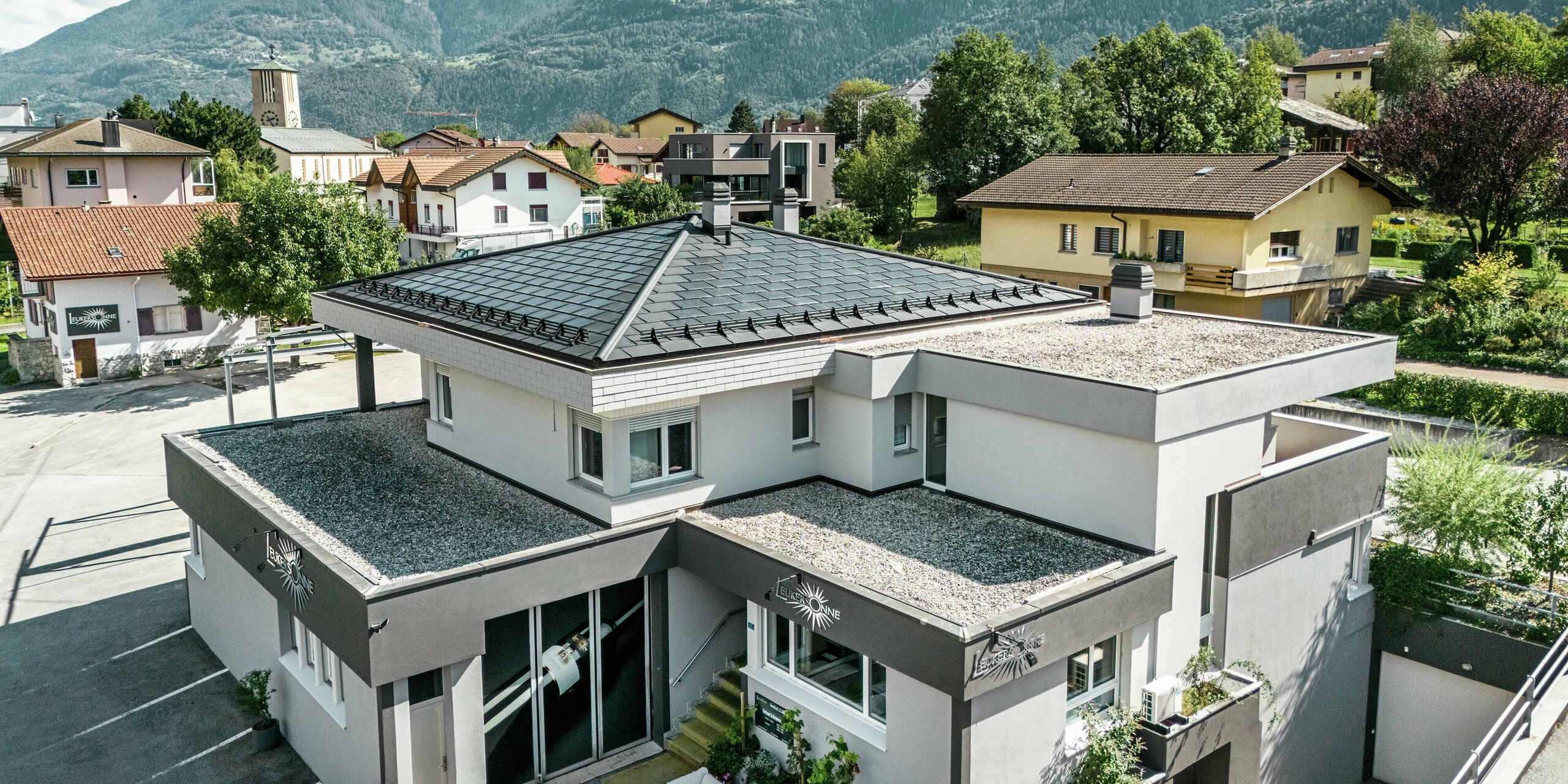 Das elegante PREFA Dach aus Aluminium verleiht der Weinkellerei Leukersonne in Susten (CH) ein modernes Erscheinungsbild und bietet optimalen Schutz vor Witterungseinflüssen. PREFA Solardachplatten sorgen für eine nachhaltige Energiegewinnung ohne das Erscheinungsbild des Zeltdaches zu beeinträchtigen. Abgerundet wird die Dachlandschaft durch PREFA Dachplatten R.16. Das erste Obergeschoss und der restliche Teil des zweiten Obergeschosses sind mit einem begehbaren Kiesbelag versehen. 