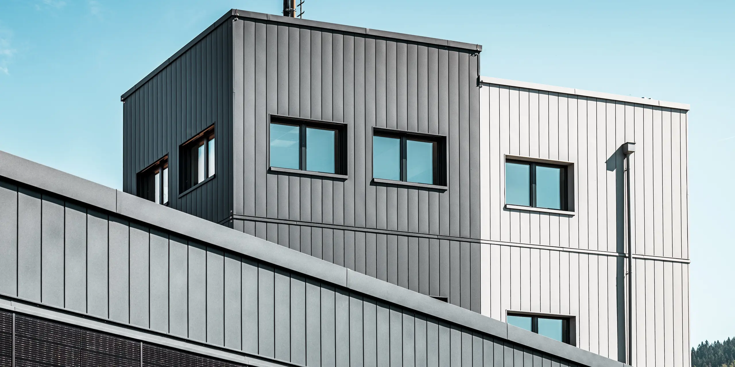 Detailansicht der Fassade des Firmengebäudes KIF Parechoc in Le Brassus mit vertikal verlegten PREFA Sidings in P.10 Anthrazit und Patinagrau. Die unterschiedlichen Grautöne betonen die kubische Architektur und setzen die präzise Linienführung wirkungsvoll in Szene. Großzügige Fensterflächen ergänzen die moderne Gestaltung, während die langlebigen PREFA Aluminiumfassaden durch Korrosionsbeständigkeit, Witterungsresistenz und geringen Wartungsaufwand überzeugen.