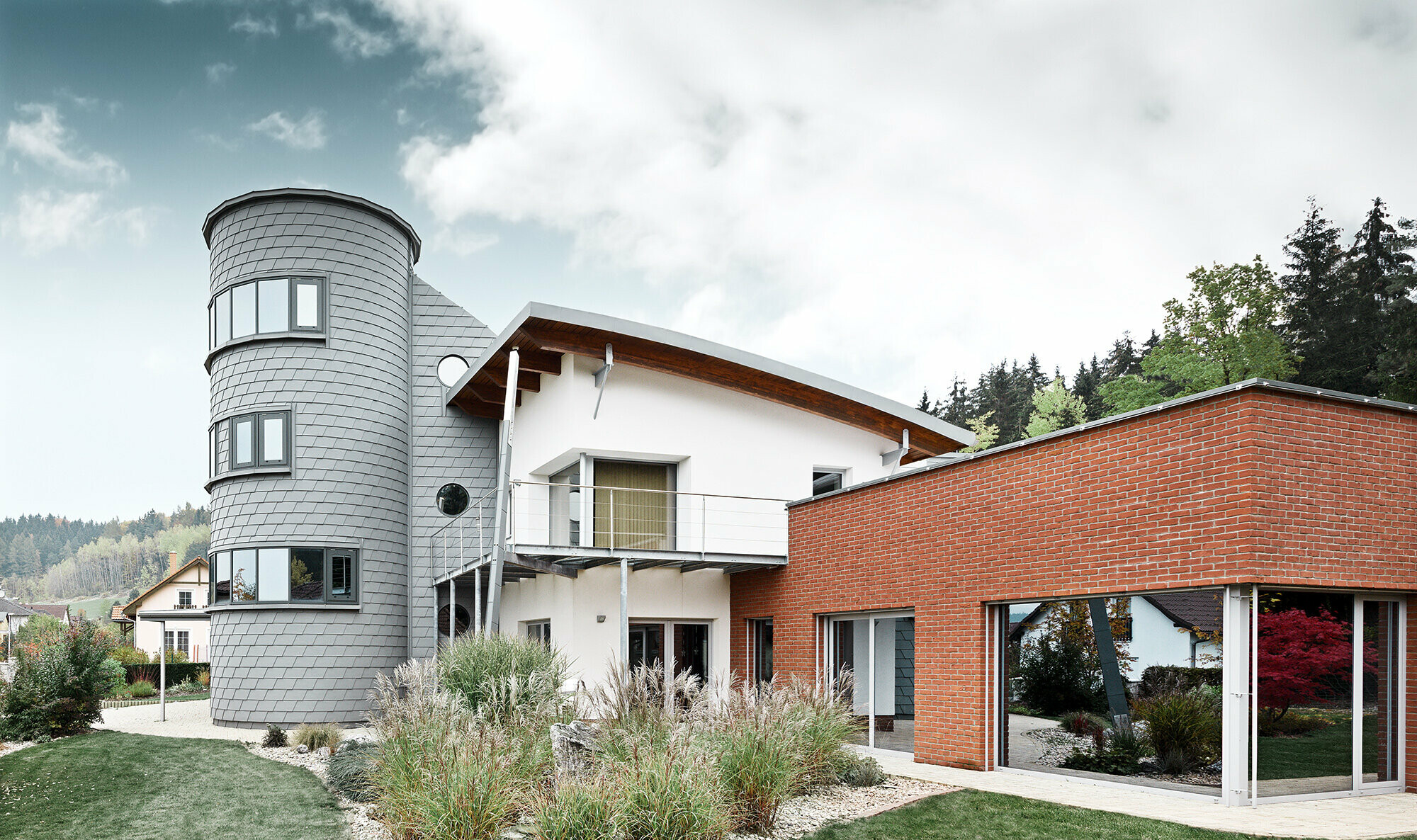 Maison individuelle avec extension de tour ; la tour ronde est revêtue du bardeau de façade PREFA couleur gris quartz 