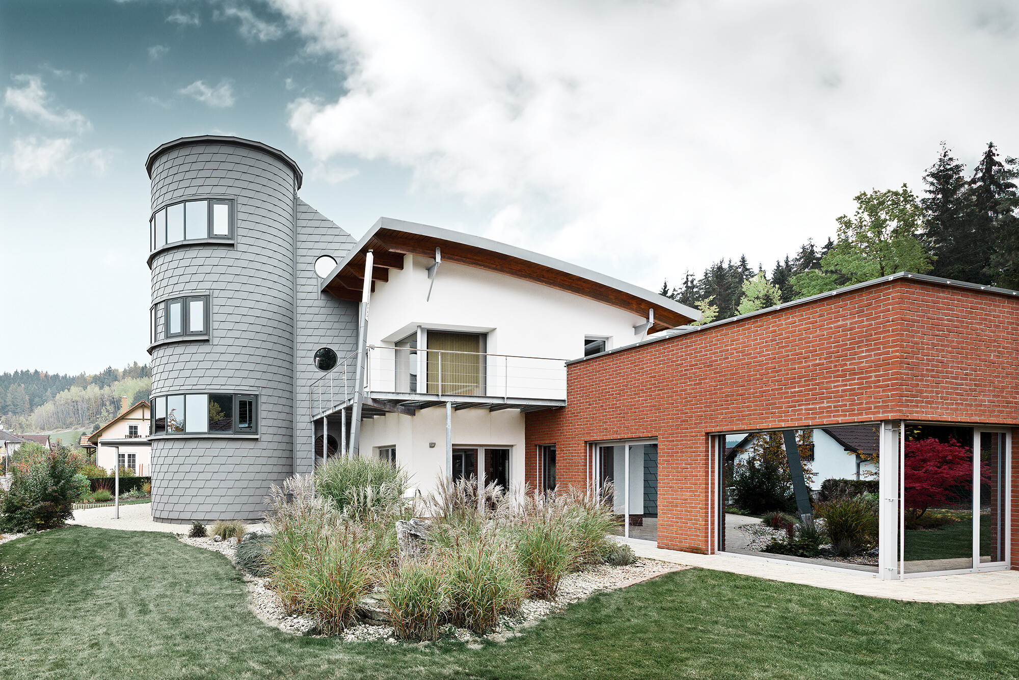 Maison individuelle avec extension de tour ; la tour ronde est revêtue du bardeau de façade PREFA couleur gris quartz 
