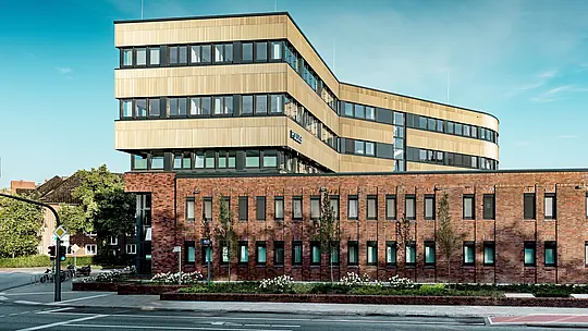 Vue panoramique du commissariat 43 à Hambourg : dominant la robuste maçonnerie de briques, l’extension moderne arbore une façade remarquable en aluminium PREFA, composée de profils extrudés « triangle » couleur bronze moyen. La surface finement texturée crée de vibrants reflets de lumière et souligne les lignes horizontales épurées et les courbes douces du bâtiment. Véritable point focal, la façade allie l’élégance architecturale aux avantages de l’aluminium PREFA : durabilité, résistance à la corrosion et quasi-absence d’entretien.