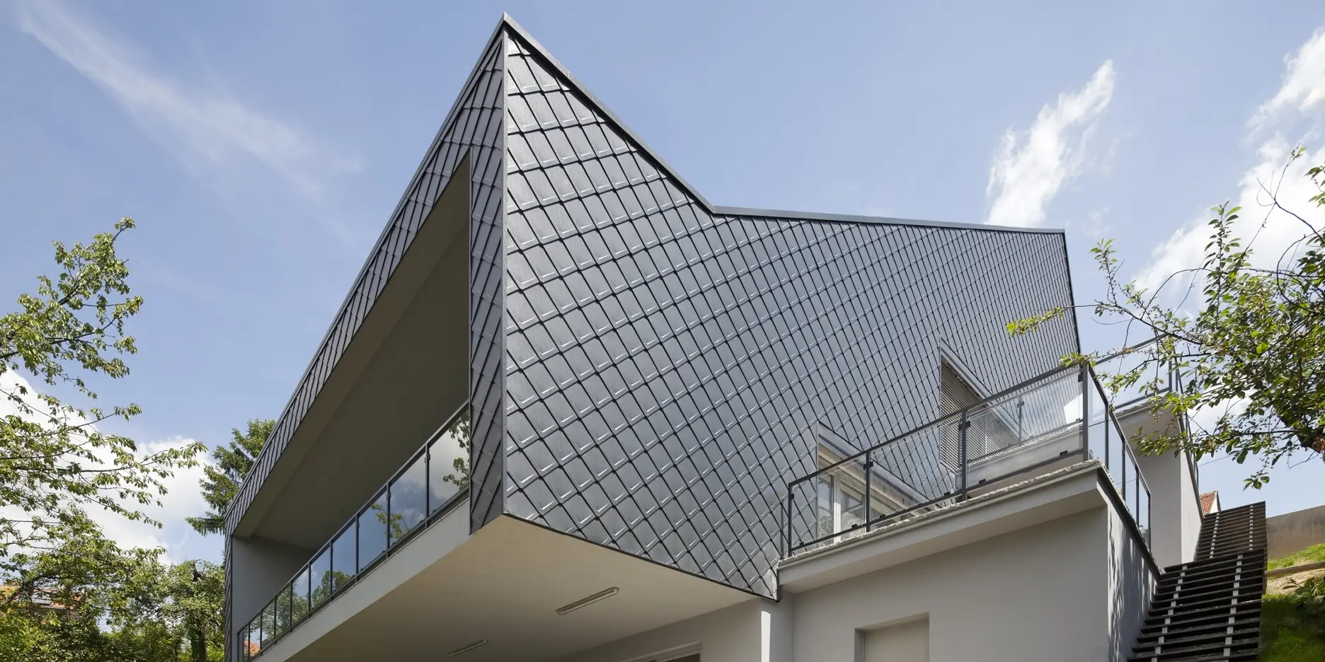 Ein modernes Wohnhaus in Zagreb, aufgenommen aus der Froschperspektive. Das stilvolle Einfamilienhaus wurde mit robusten PREFA-Blechrauten in Anthrazit verkleidet. Die hochwertige Aluminiumhülle sorgt für Langlebigkeit und ein elegantes Erscheinungsbild. Die überdachte Terrasse ist das Highlight der Gebäuderückseite.
