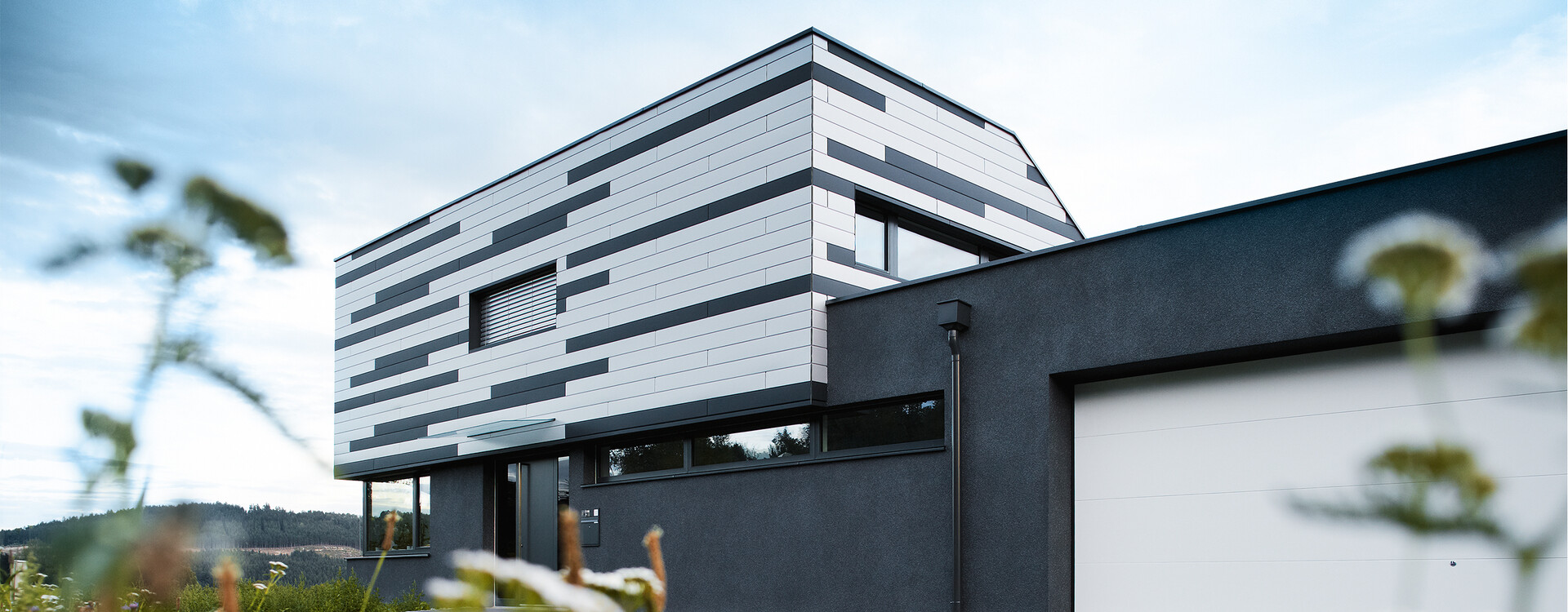 Maison individuelle moderne présentant une conception de façade créative. Les Sidings PREFA couleur argent et anthracite mat ont été posés mélangés.