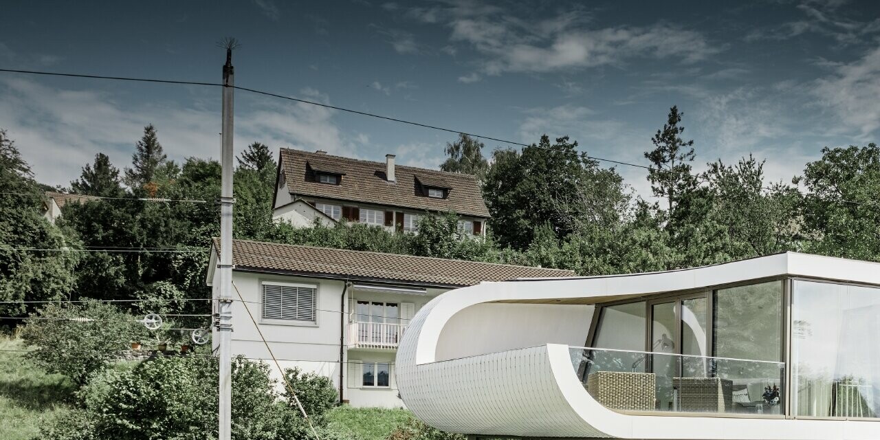 Maison individuelle très moderne conçue par l’architecte Stefan Camenzind de Zurich ; une bande ondulée relie les différents étages entre eux. Les courbures ont été habillées avec le losange de toiture PREFA, en petit format, couleur blanc pur. La maison présentant de nombreuses et vastes surfaces vitrées, elle donne une grande impression d’ouverture.