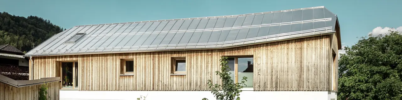 Seitliche Ansicht des Einfamilienhauses in Pruggern eingedeckt mit PREFALZ in der Farbe Naturblank bei Sonnenschein