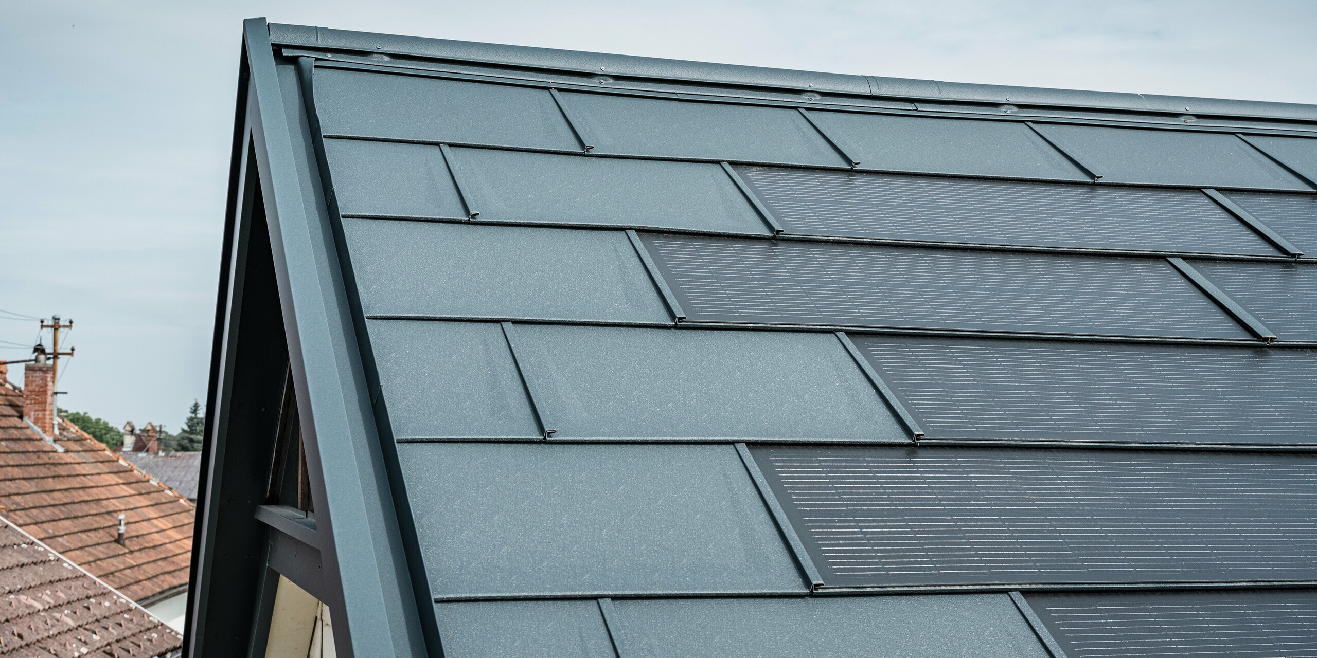 Vue détaillée du toit d'une maison équipée de la tuile solaire innovante PREFA. Les tuiles avec cellules photovoltaïques intégrées sont présentées dans un élégant anthracite. La surface homogène s'intègre parfaitement dans le toit et assure ainsi un aspect moderne et épuré. Le système de toiture innovant permet une utilisation efficace de l’énergie sans compromettre l’esthétique.