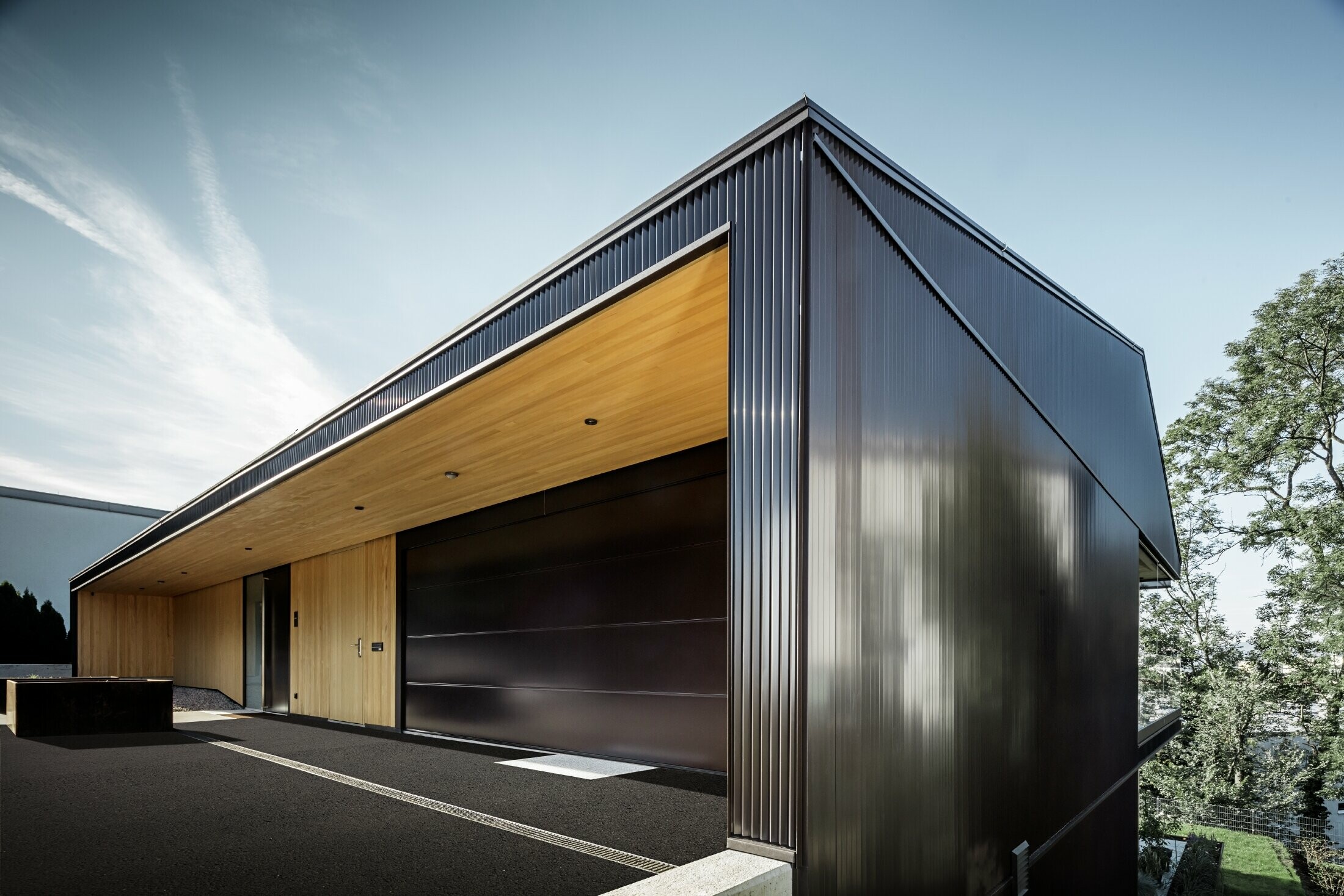 Entrée de garage d’une maison individuelle, la façade est recouverte de profils triangle PREFA couleur brun foncé. 
