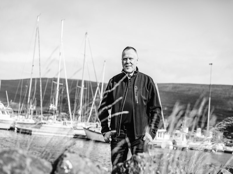 Der isländische Architekt Tryggvi Tryggvason steht im Freien vor einer Landschaft. Im Hintergrund sind Segelschiffe zu sehen.