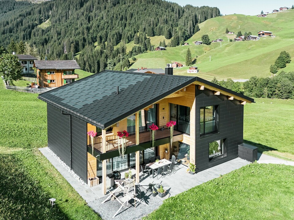 Cette élégante maison individuelle située dans les environs vallonnés d'Ascharina (Suisse) montre comment l'aluminium et le bois peuvent être parfaitement combinés. Les robustes panneaux de façade PREFA Siding.X en noir P.10 s'harmonisent avec le toit composé de panneaux solaires PREFA et de panneaux de toiture R.16 dans le même revêtement de couleur. L'enveloppe en aluminium durable protège le bâtiment de manière fiable contre les défis du climat alpin.