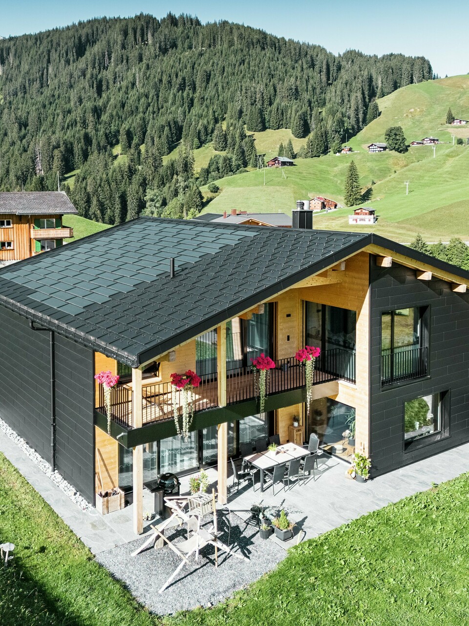Cette élégante maison individuelle située dans les environs vallonnés d'Ascharina (Suisse) montre comment l'aluminium et le bois peuvent être parfaitement combinés. Les robustes panneaux de façade PREFA Siding.X en noir P.10 s'harmonisent avec le toit composé de panneaux solaires PREFA et de panneaux de toiture R.16 dans le même revêtement de couleur. L'enveloppe en aluminium durable protège le bâtiment de manière fiable contre les défis du climat alpin.