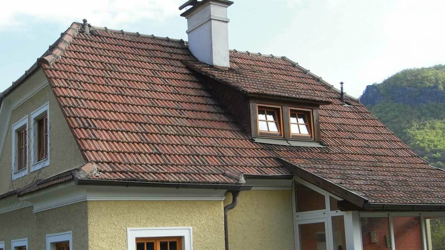 Altes Einfamilienhaus vor der Dachsanierung mit Ziegeldach und rauer, gelber Putzfassade