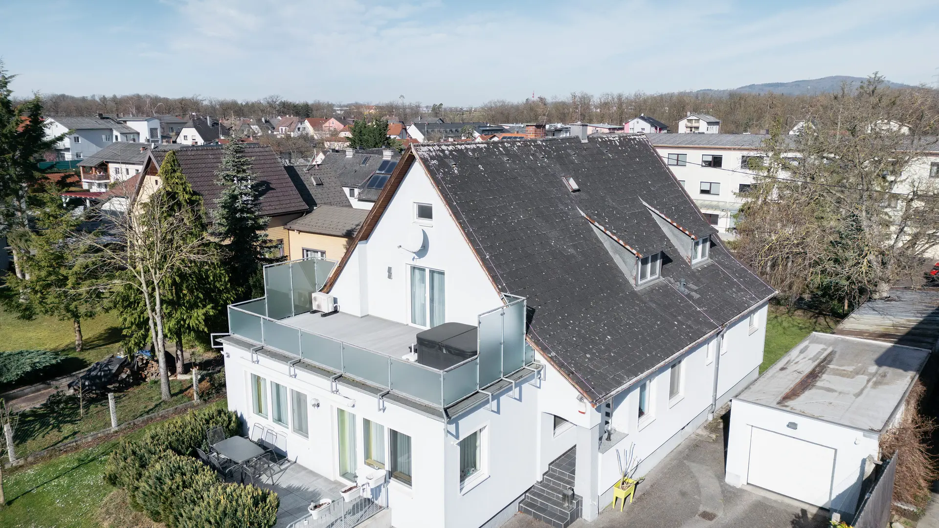 Vue aérienne d'un immeuble doté d'une vieille toiture en Eternit recouverte de saleté et de lichens. Aucune installation solaire n'est visible sur la toiture. Le balcon au premier plan est doté d'une balustrade en verre et se trouve à l'étage supérieur de l'immeuble.