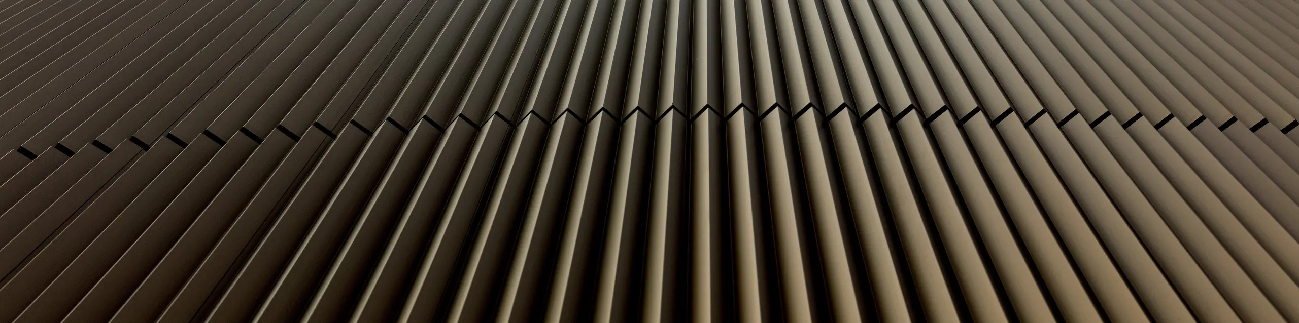 Gros plan saisissant sur la façade en aluminium PREFA du commissariat 43 à Hambourg : les profils extrudés verticaux « triangle », couleur bronze moyen, attirent immédiatement le regard et, grâce à leurs nervures précises, créent un fascinant jeu d’ombre, de lumière et de profondeur. La géométrie légèrement incurvée souligne le dynamisme architectural. L’aluminium PREFA séduit par sa haute résistance à la corrosion, son extrême durabilité et ses exigences minimales d’entretien : une solution durable pour des façades sophistiquées et design.